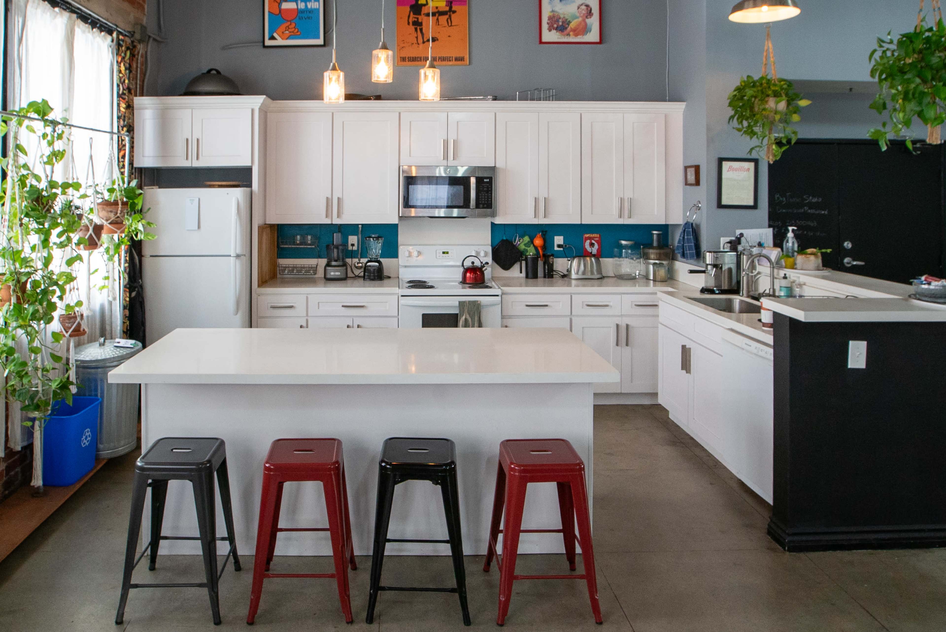 A modern kitchen with white cabinets, a central island, and four metal stools in front of it.