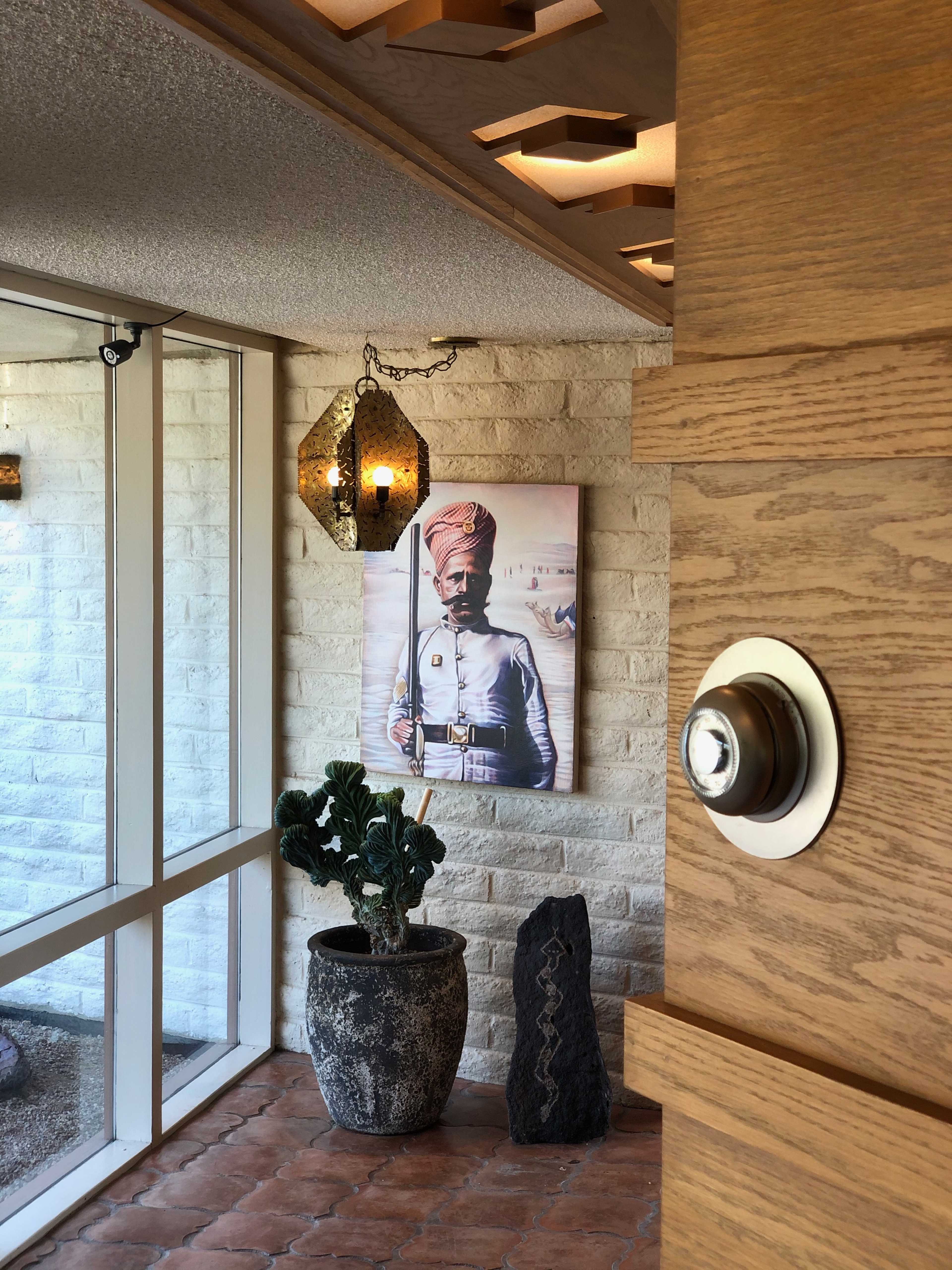 An indoor space with a potted plant, a large framed portrait of a man in traditional attire, and decorative lanterns hanging from the ceiling.