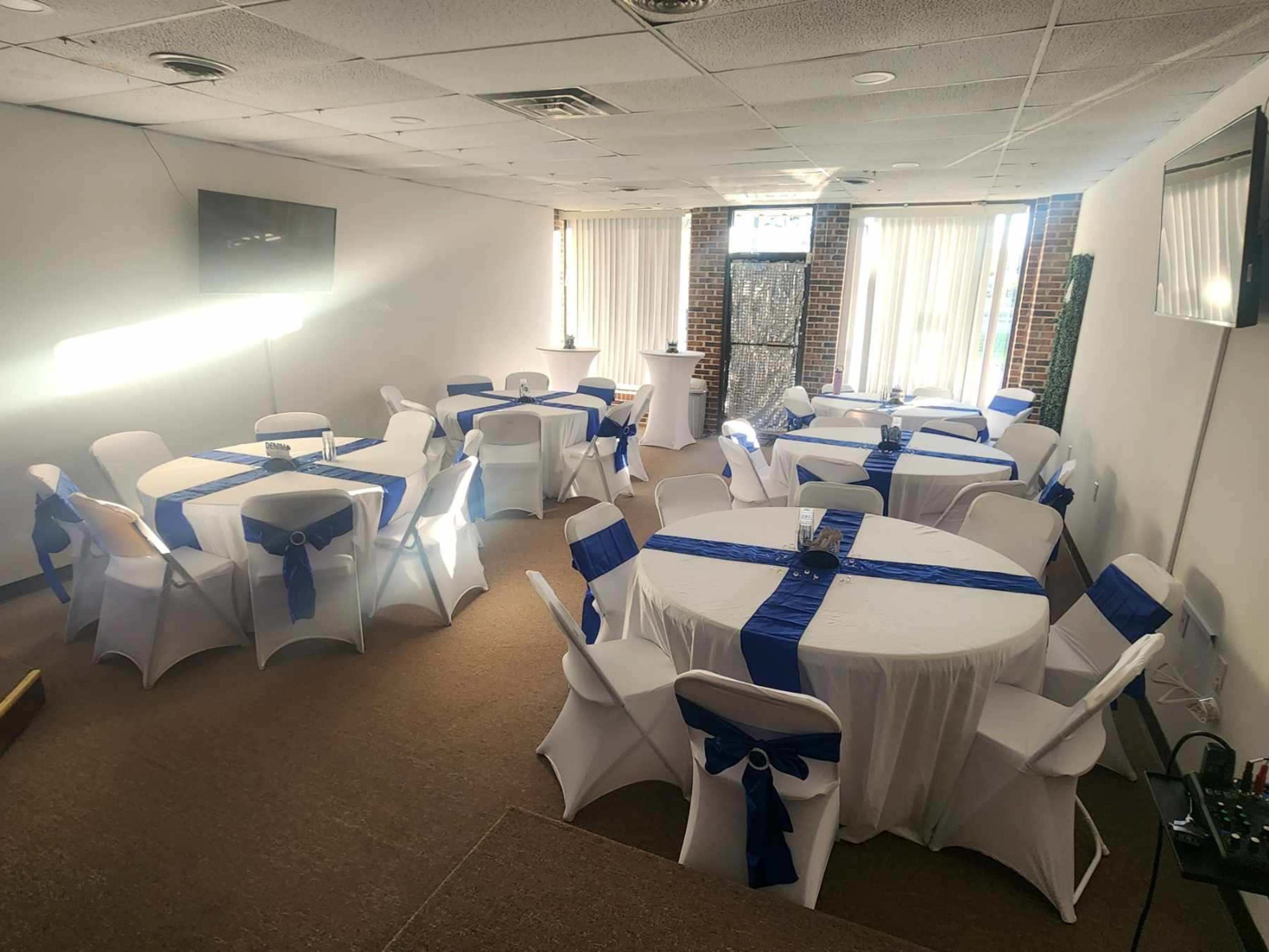 The image shows a banquet hall arranged with several tables covered in white tablecloths and blue ribbons, set up for an event.