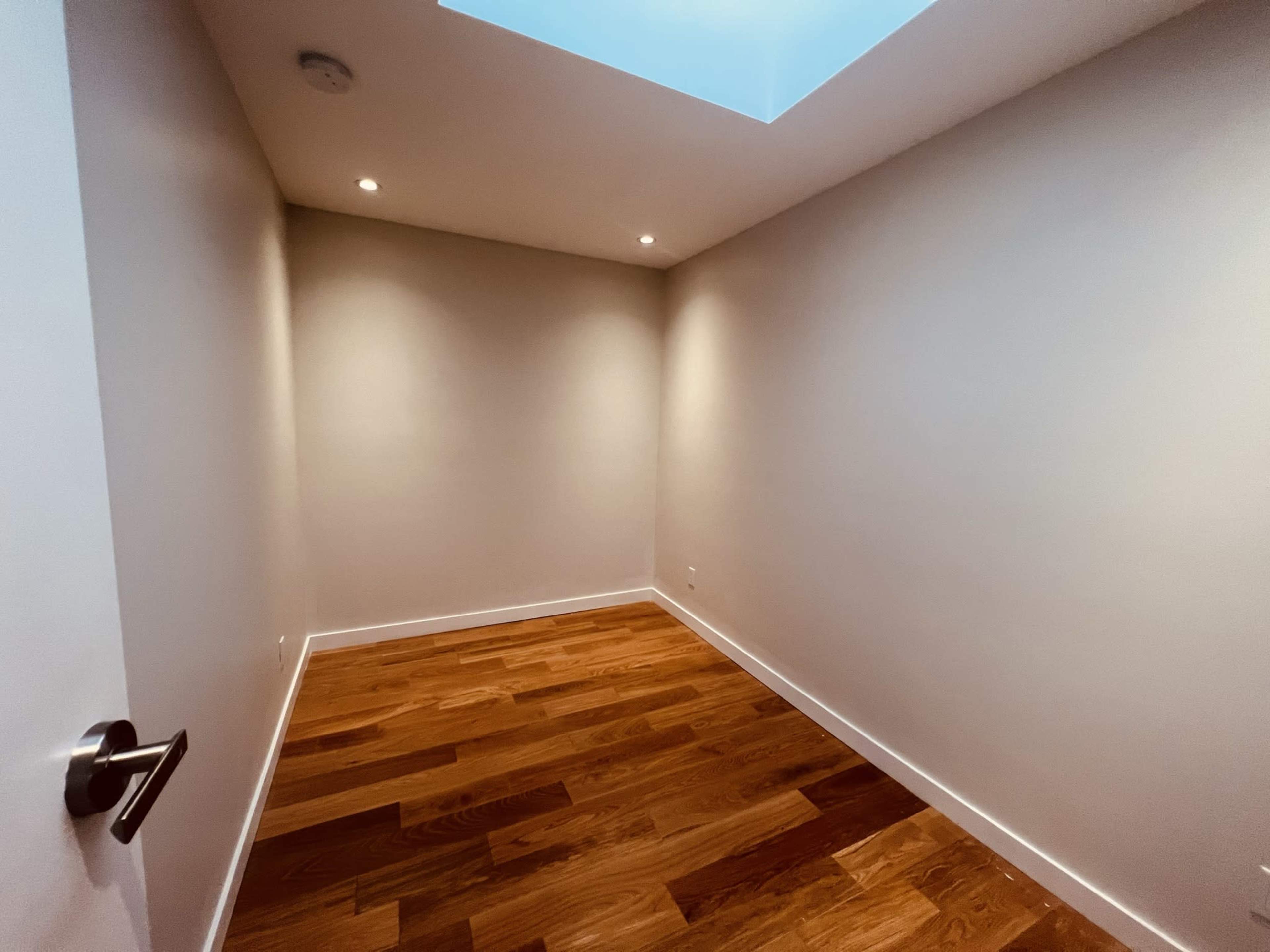 An empty room with wooden flooring and a skylight above.