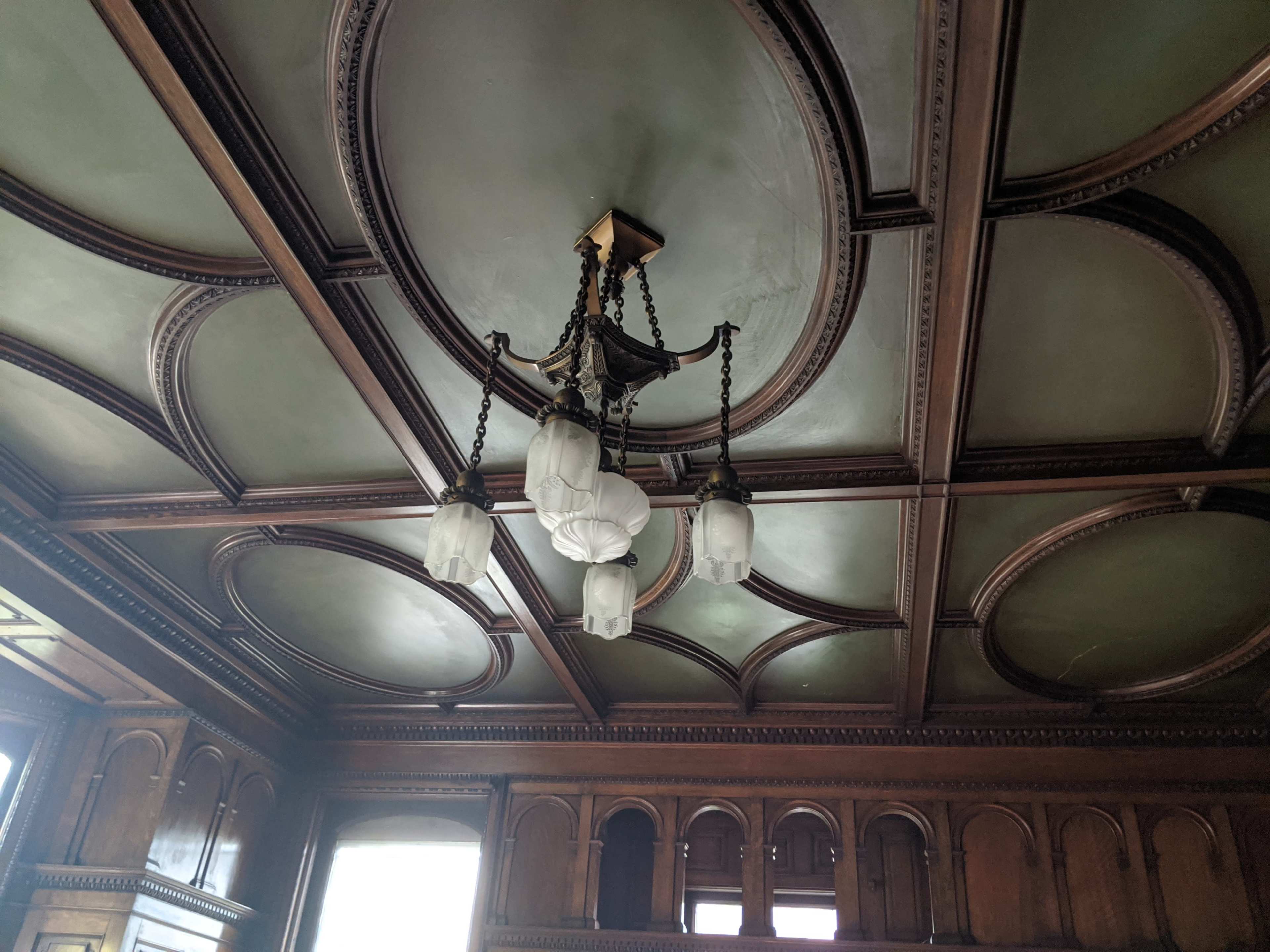 An ornate ceiling with decorative wood paneling and a chandelier with five glass shades.