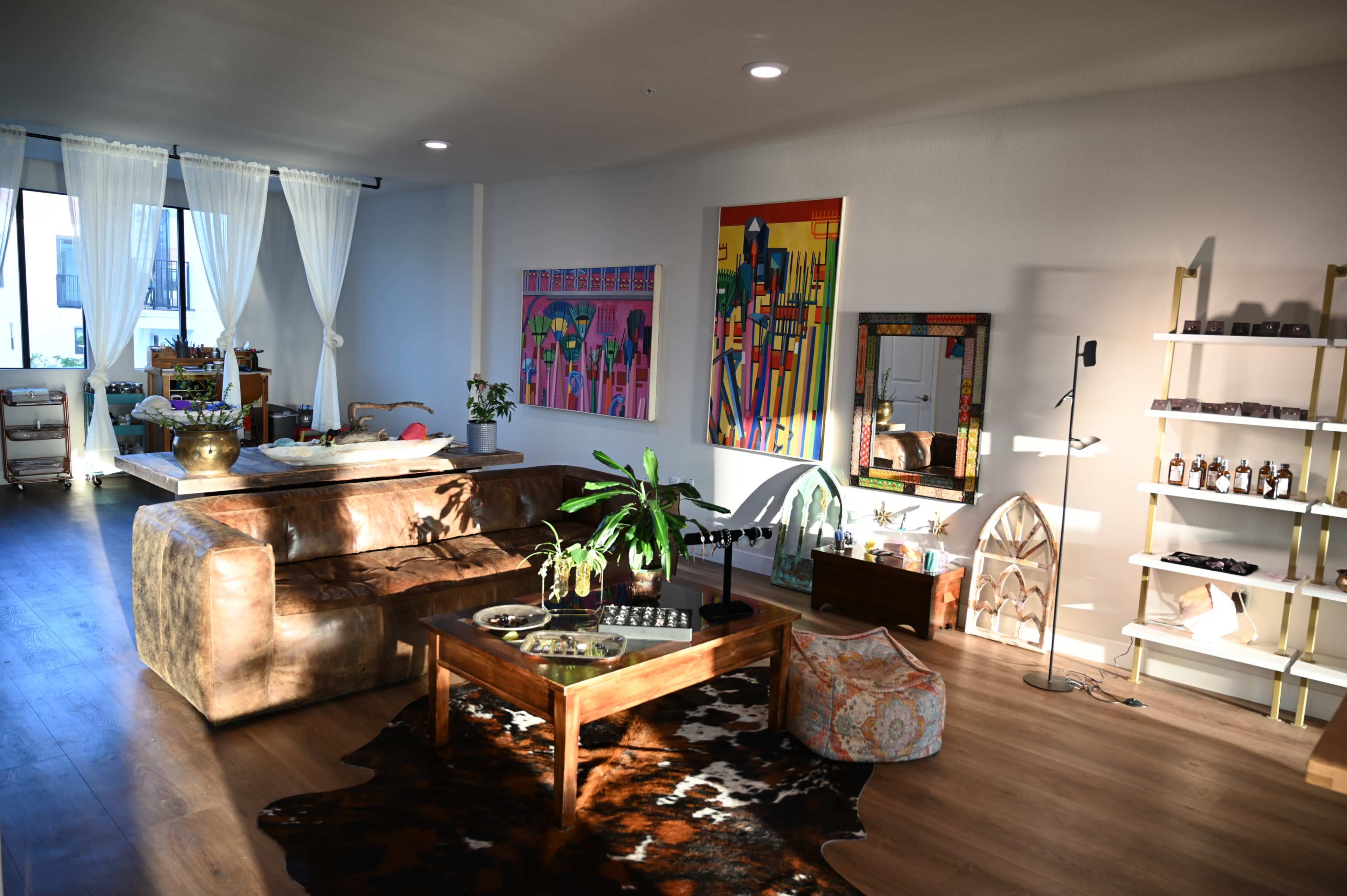 The image shows a spacious living room with a large brown sofa, a wooden coffee table, colorful artwork on the walls, and a variety of decorative items throughout the space.