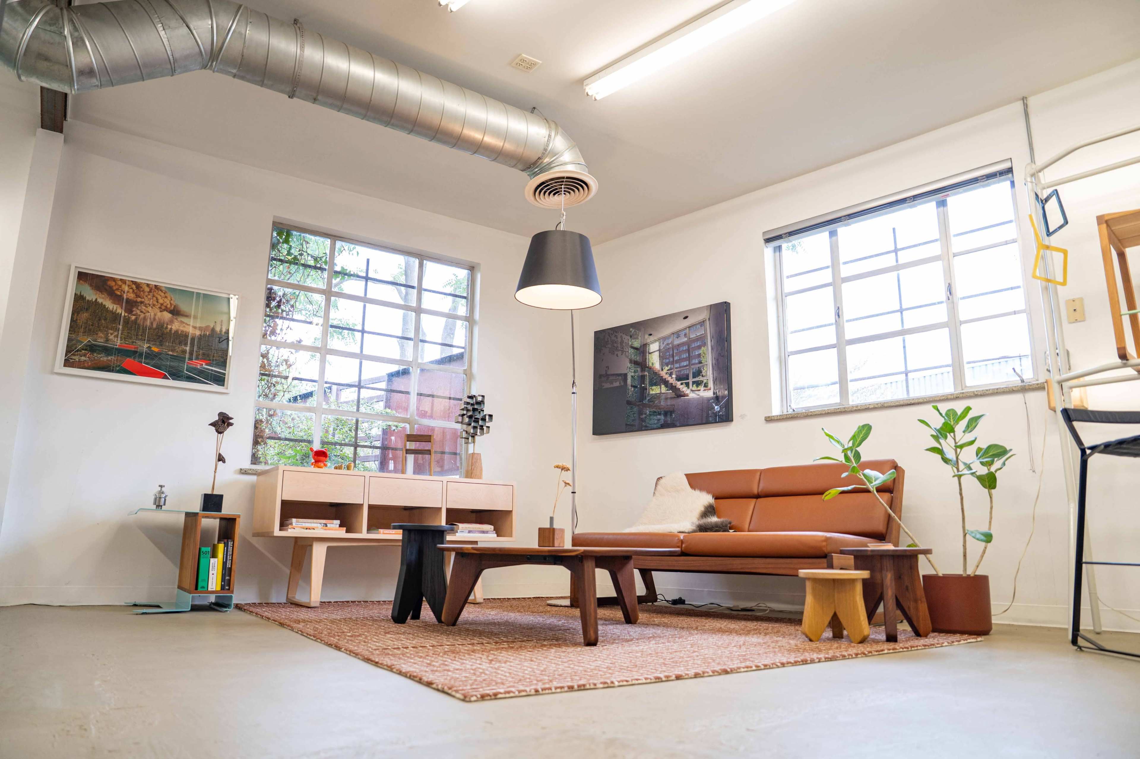 The image shows a modern living room with a brown sofa, a coffee table, decorative plants, and artwork on the walls.