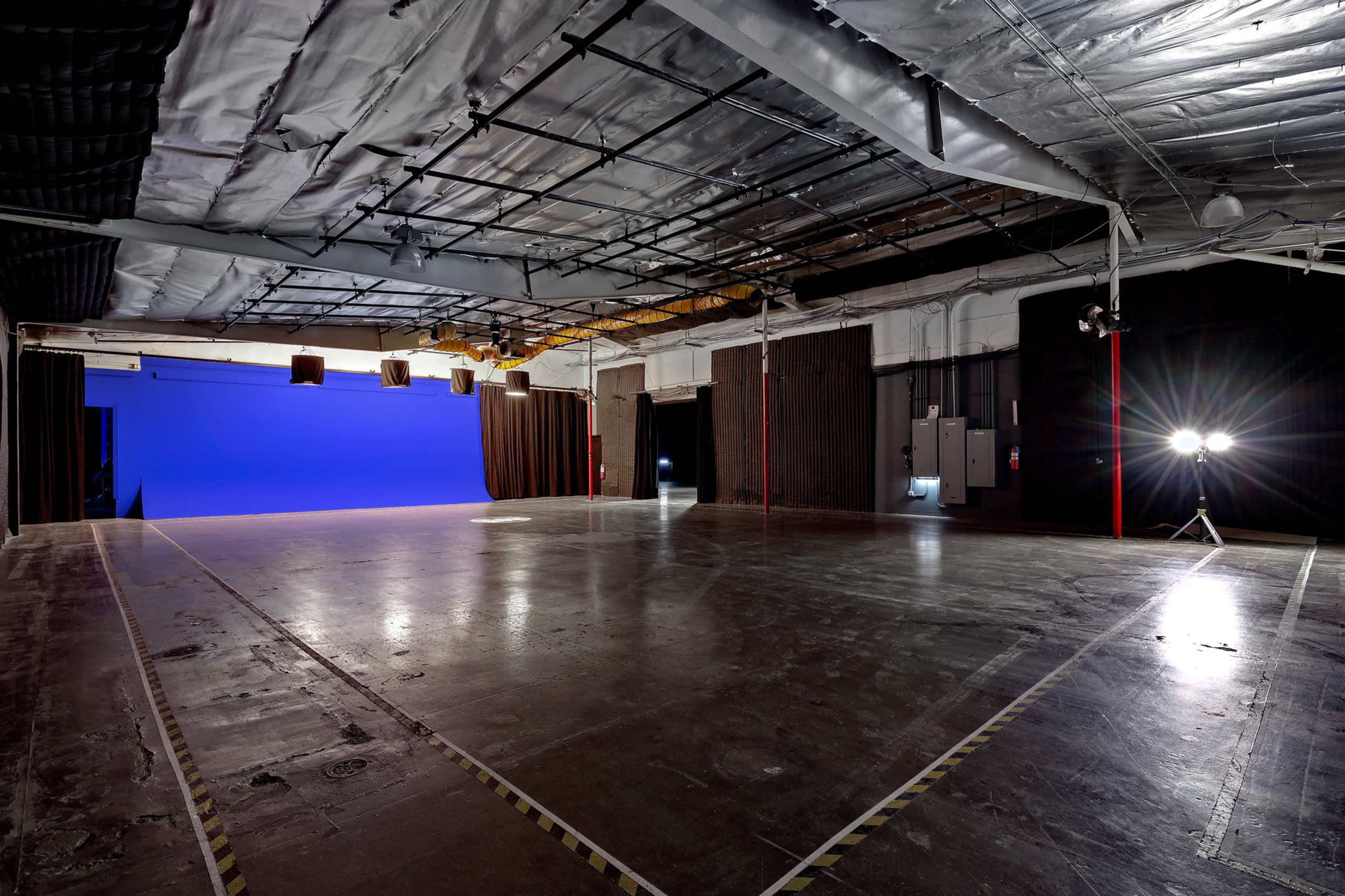 A large empty studio space with a blue backdrop and overhead lighting.