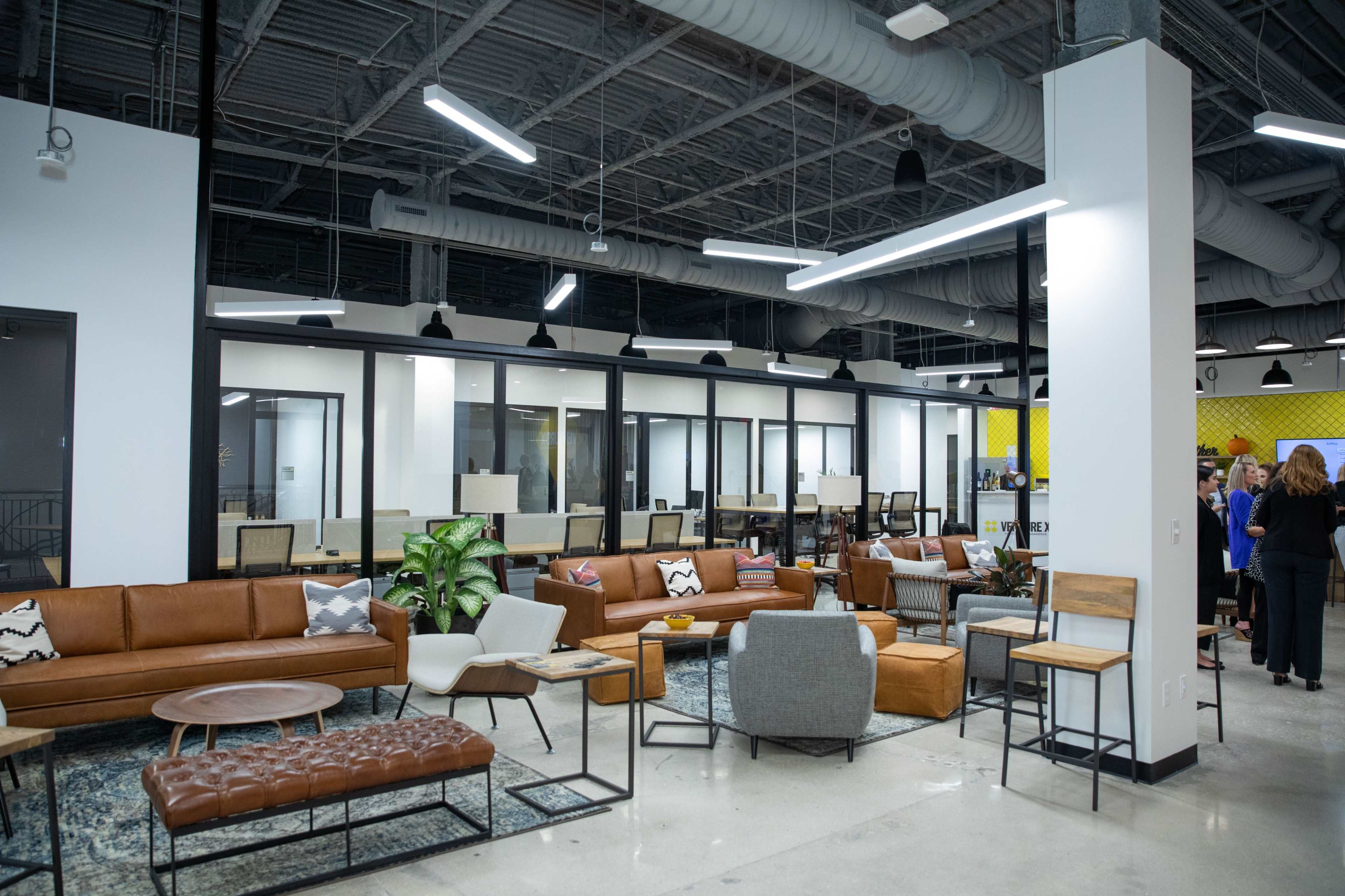 The image shows a modern office space featuring leather couches, tables, and glass-walled meeting rooms.