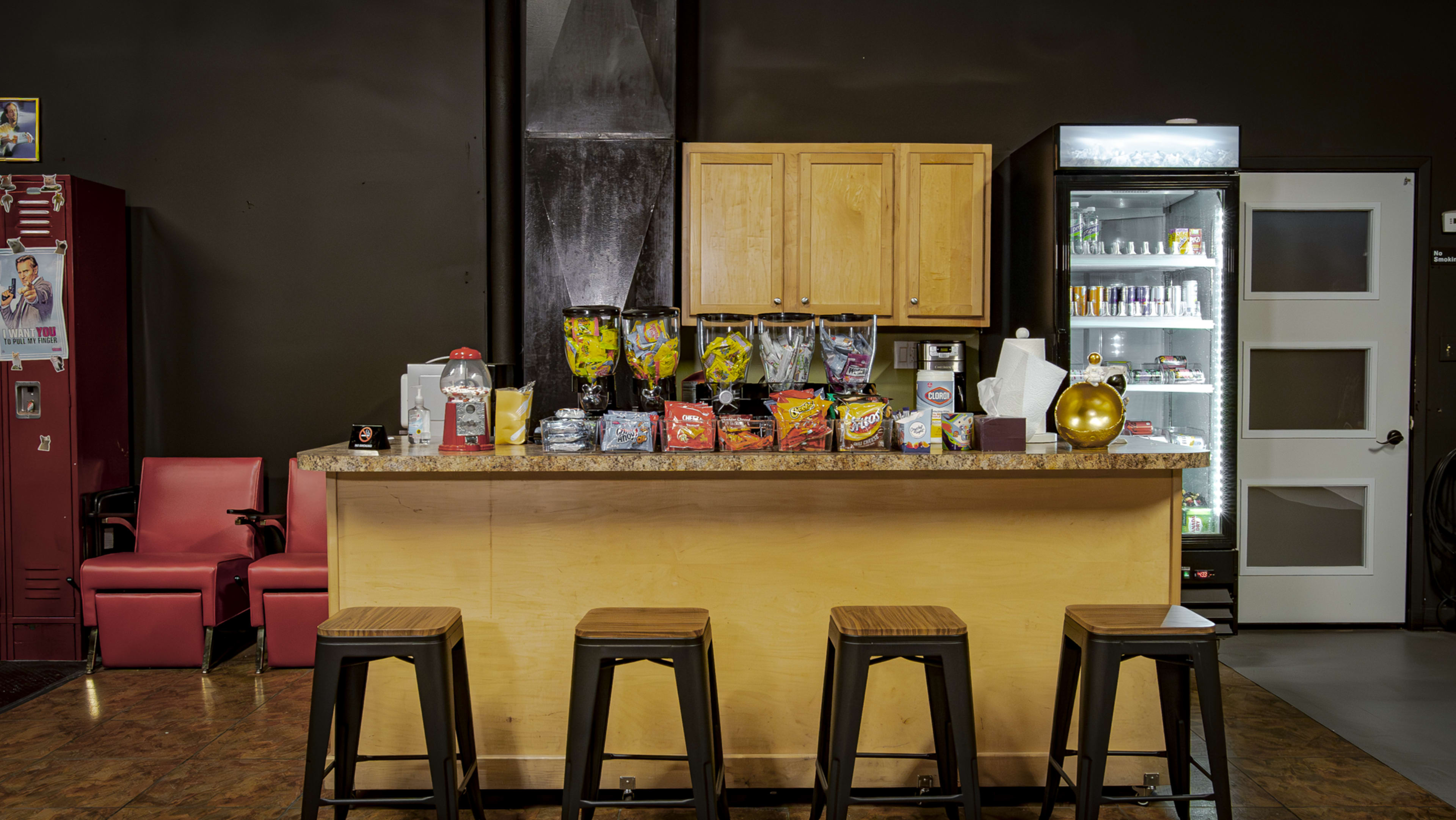 A modern snack bar features a countertop with various snacks and drinks, backed by a refrigerator and lockers.