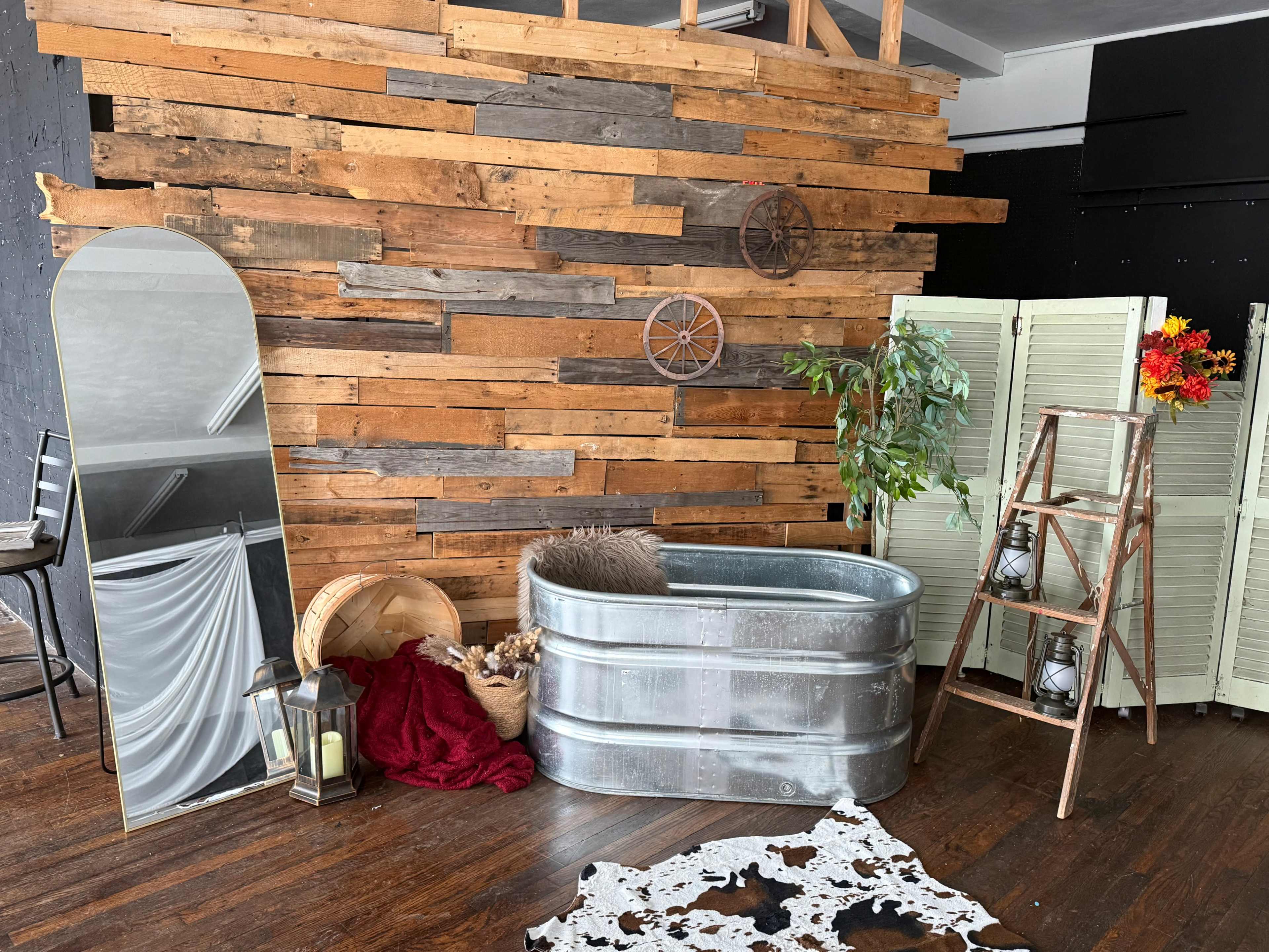 The image features a rustic interior scene with a galvanized tub, a large mirror, a wooden ladder, and decorative elements against a backdrop of wooden planks.