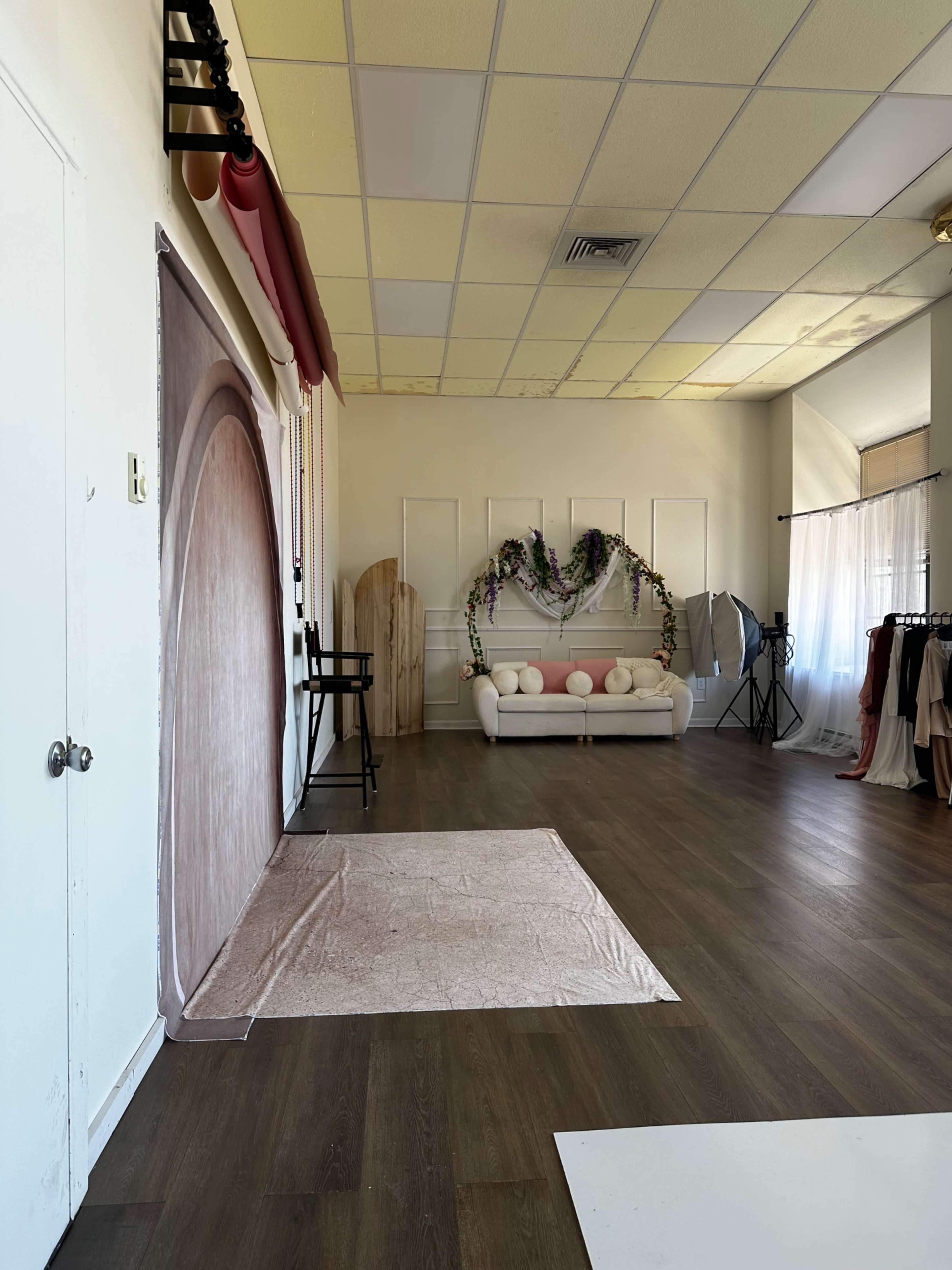 The image shows a spacious photography studio with a light-colored backdrop, a white couch, and various props arranged around the room.