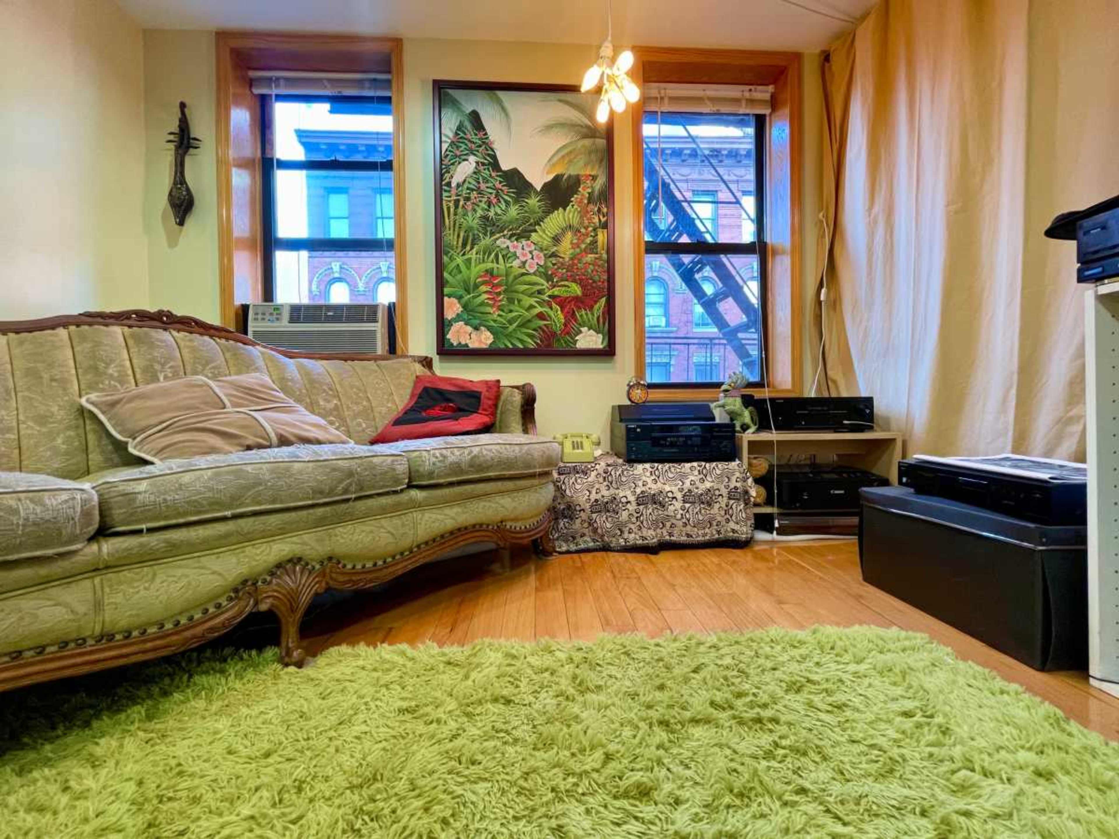 The living room features a vintage sofa, a large tropical-themed artwork on the wall, and an assortment of audio equipment arranged on the floor.