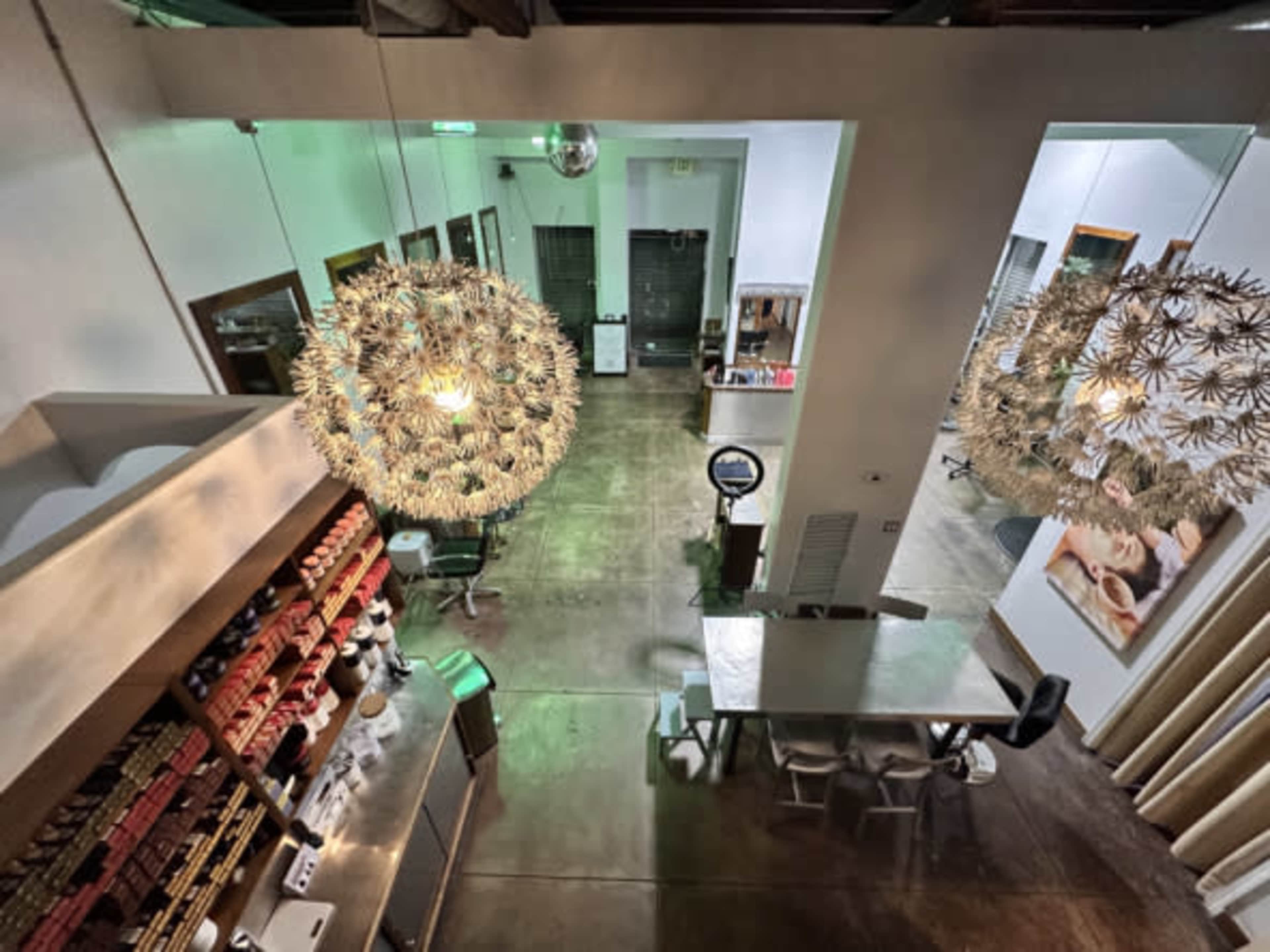 The image shows a modern café interior with large decorative light fixtures, a central communal table, and shelves displaying various products.