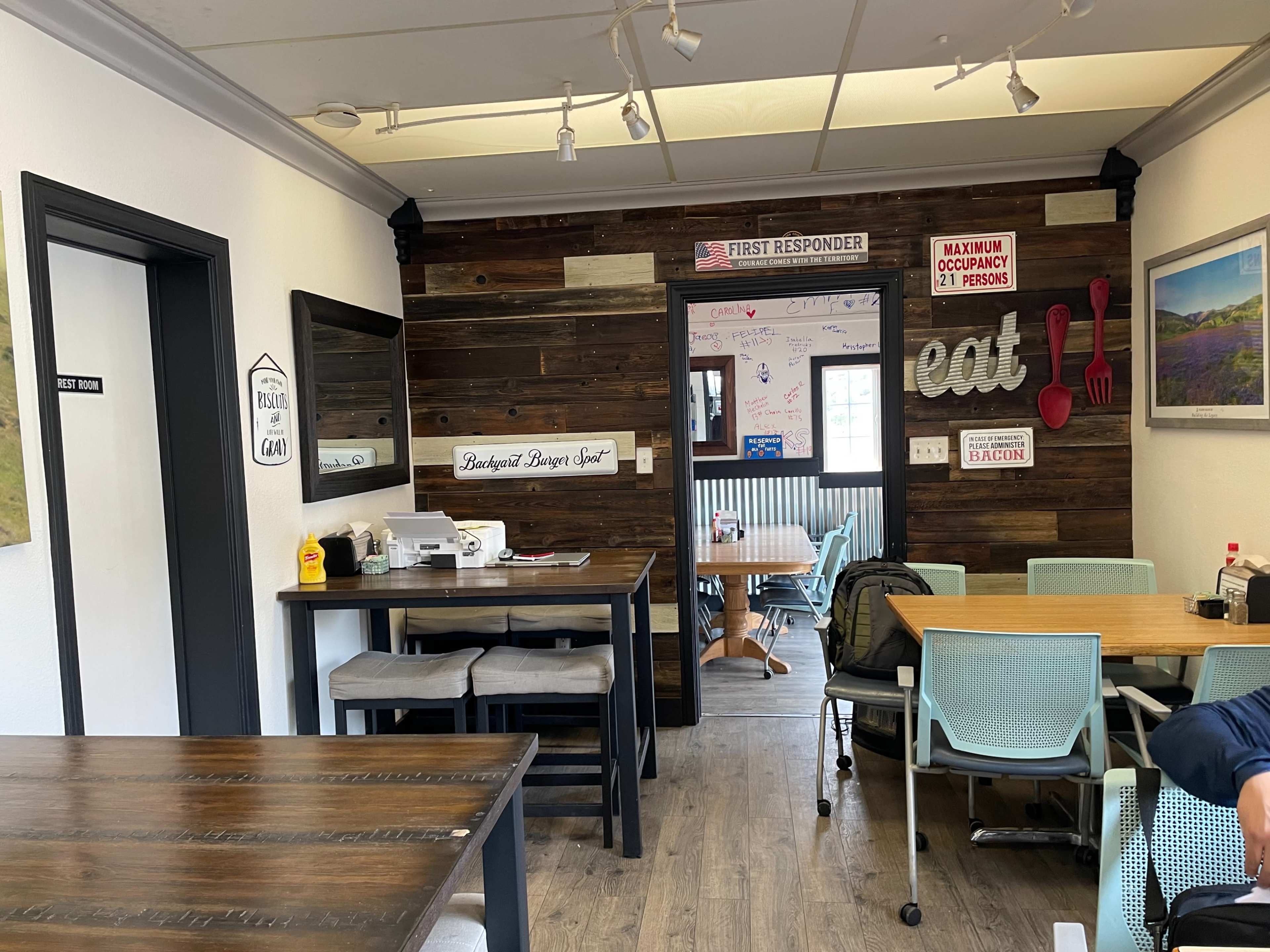 The interior of a casual dining area with wooden tables, plastic chairs, and various wall decorations including signs and artwork.
