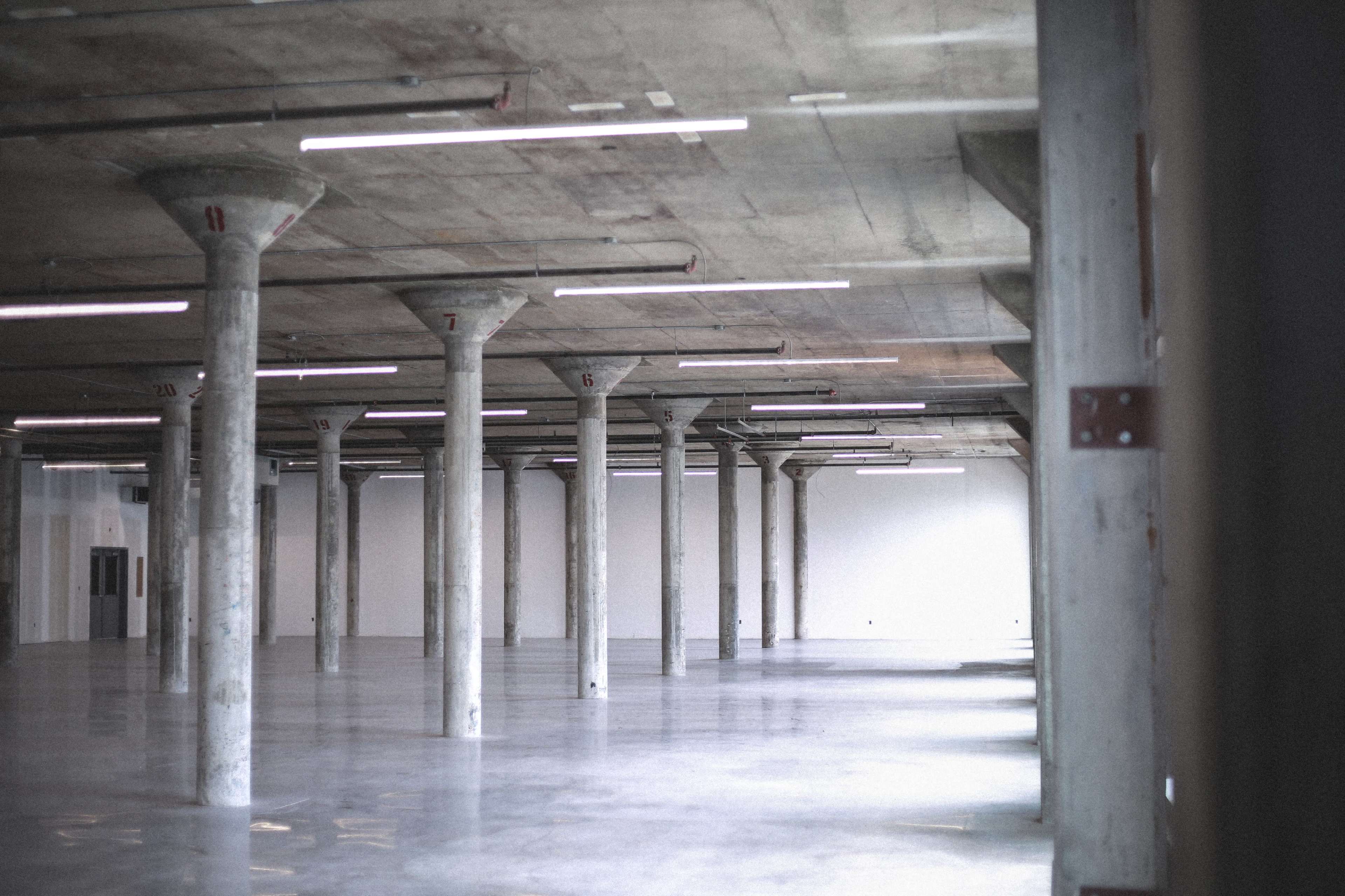An expansive, empty industrial space features concrete pillars and polished floors under overhead lighting.