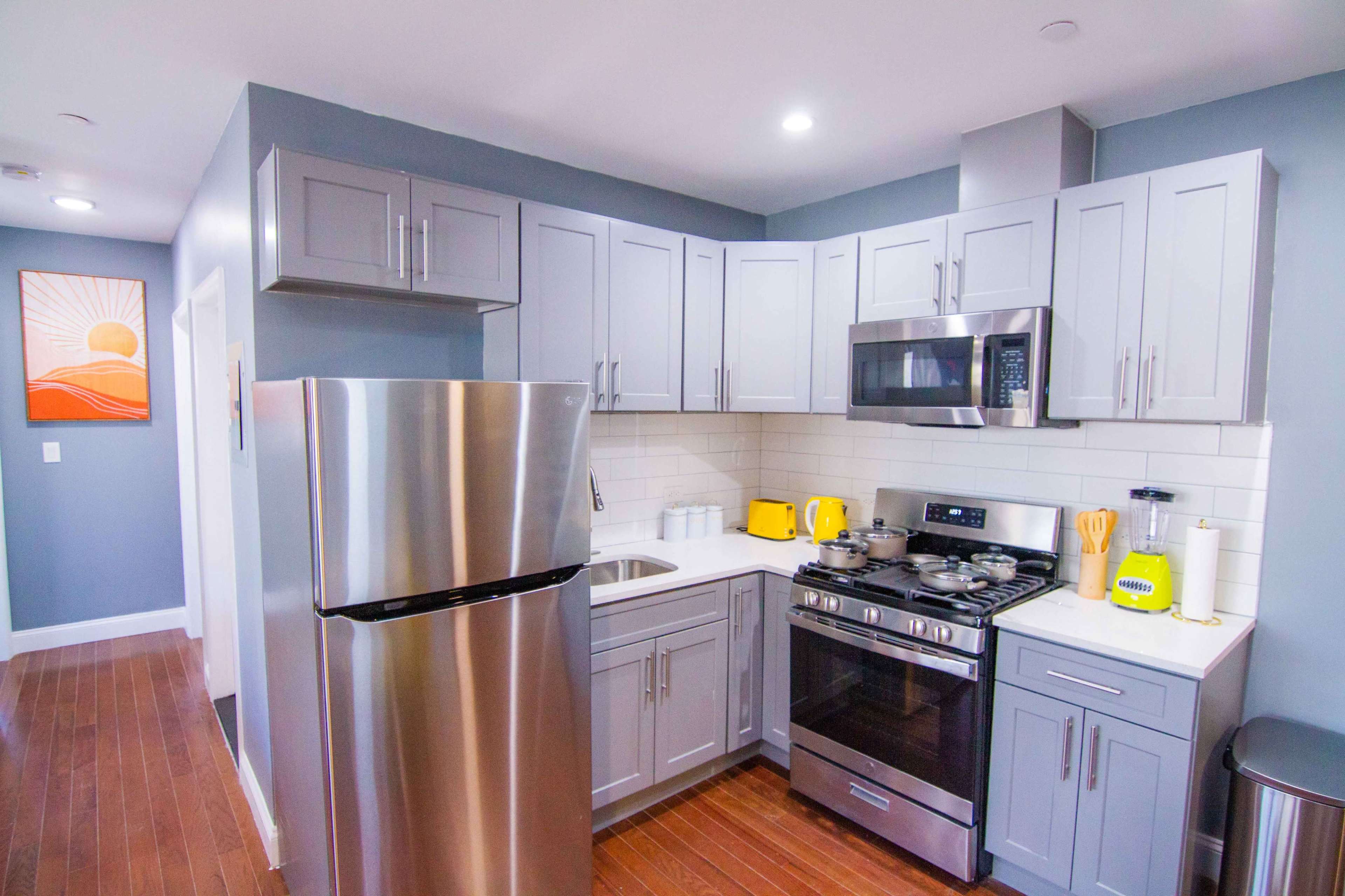 A modern kitchen with stainless steel appliances, gray cabinets, and wooden flooring.
