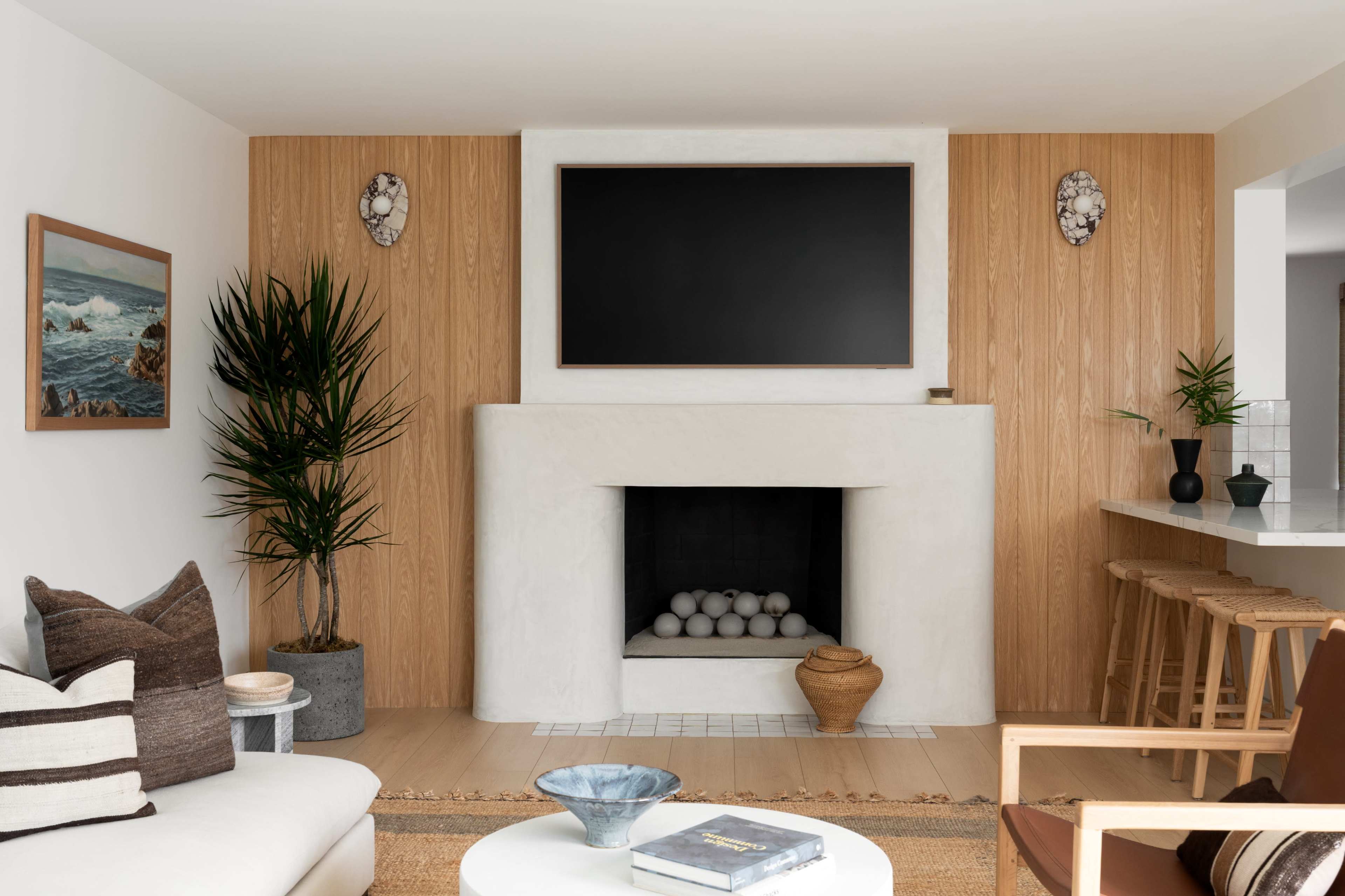 The modern living room features a white fireplace with a dark television mounted above it, surrounded by wooden paneling and decorative plants.