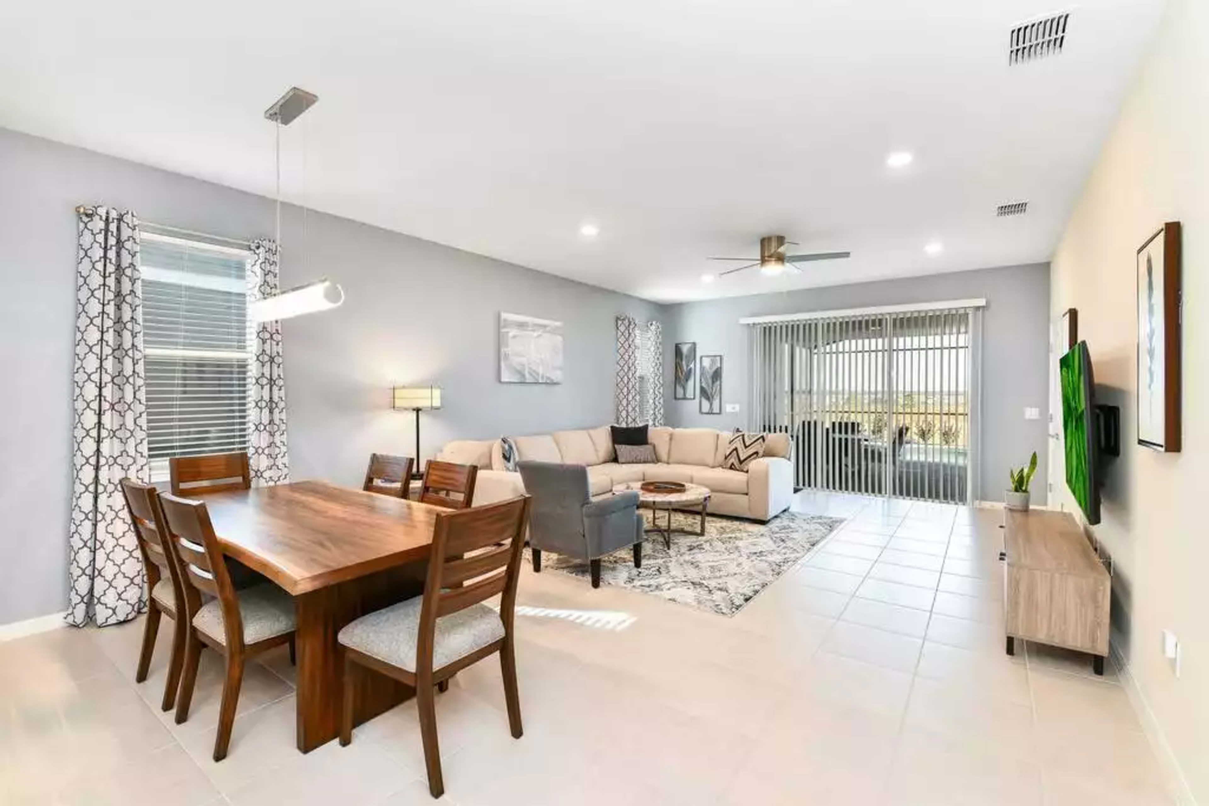 A modern living space featuring a dining area with a wooden table and chairs, a beige sectional sofa, and sliding glass doors leading to a patio.