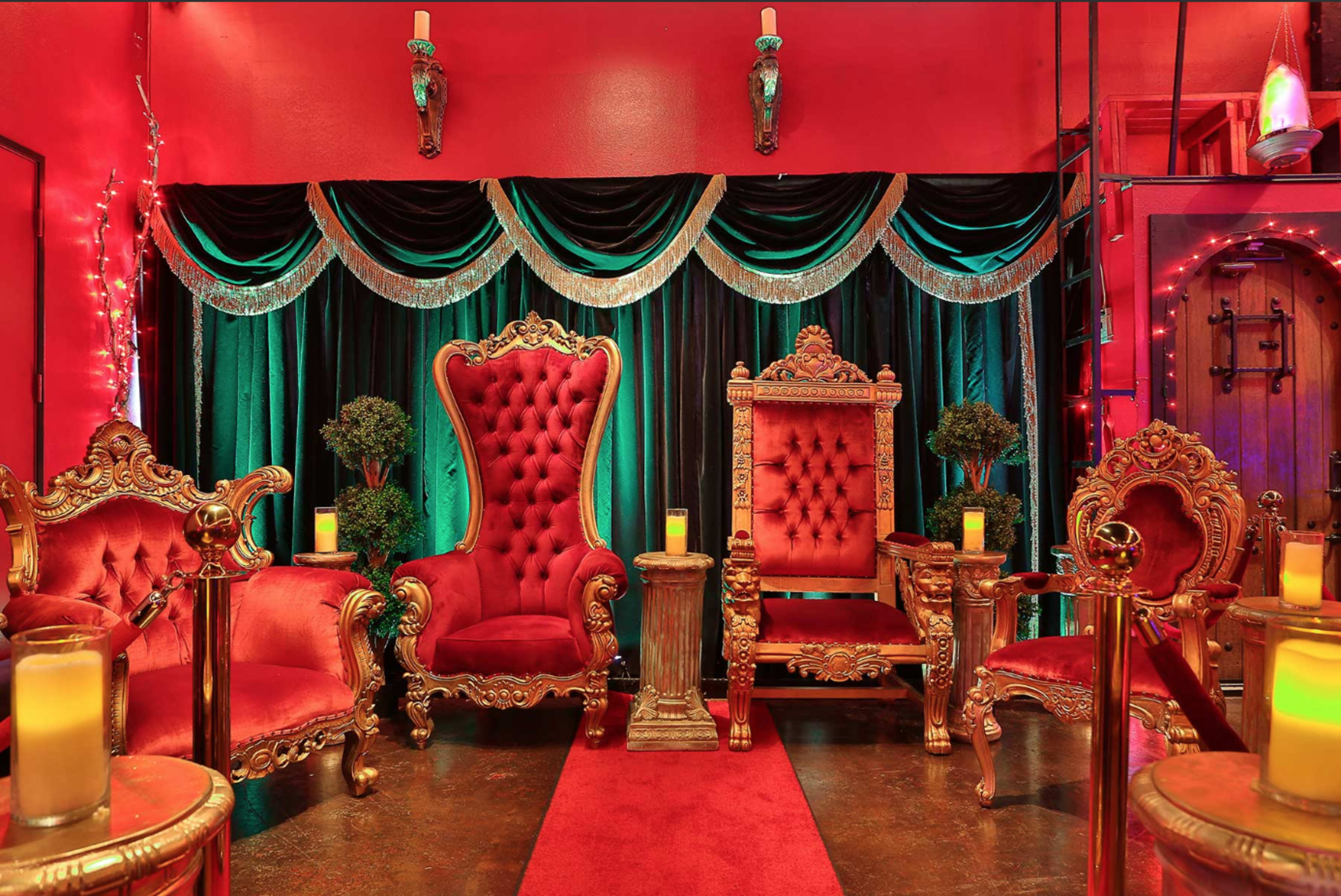 An opulent seating area with two ornate red and gold armchairs, flanked by green and black drapery and illuminated by soft candlelight.