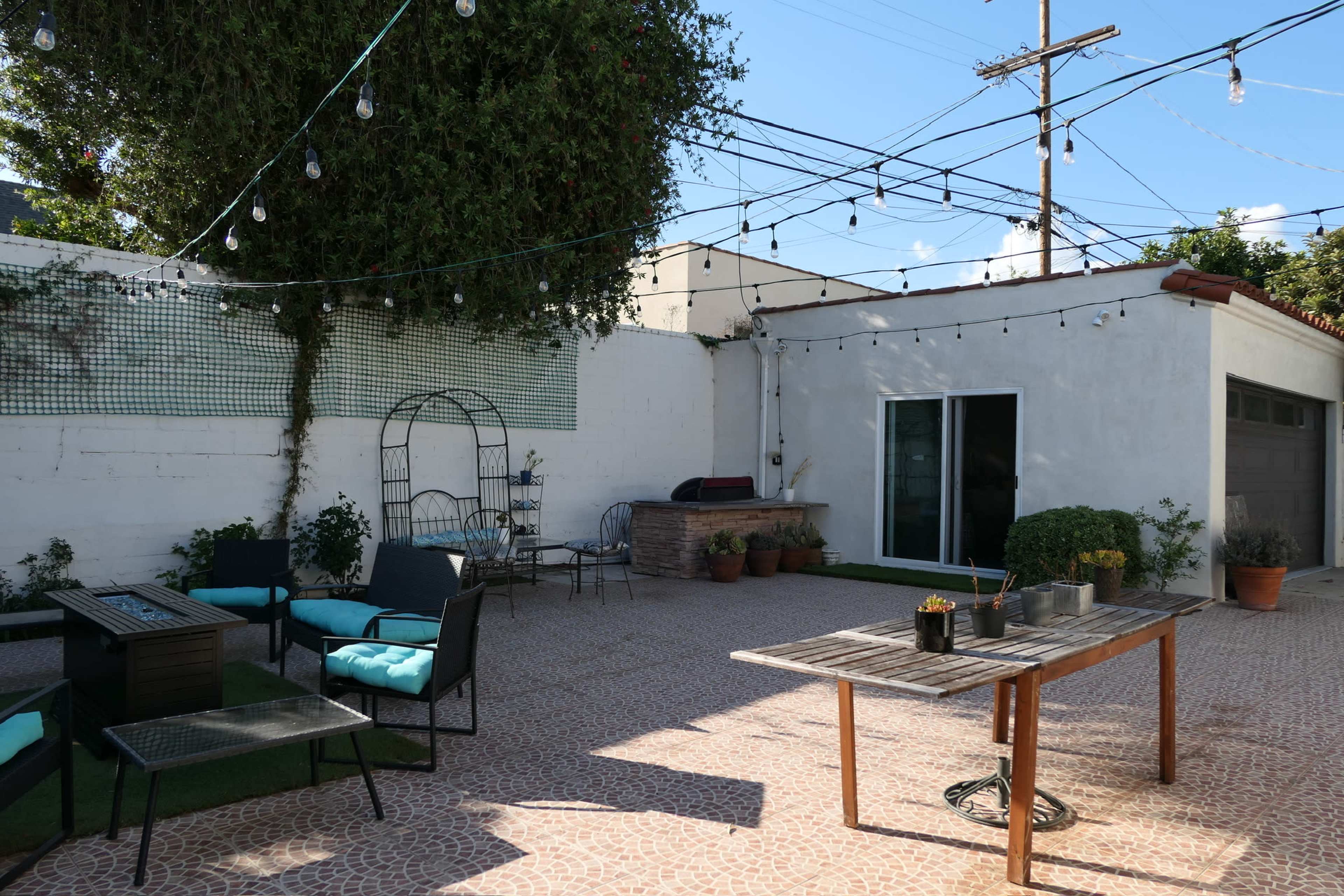A patio area featuring outdoor seating, a table, and string lights, with a wall and garage in the background.