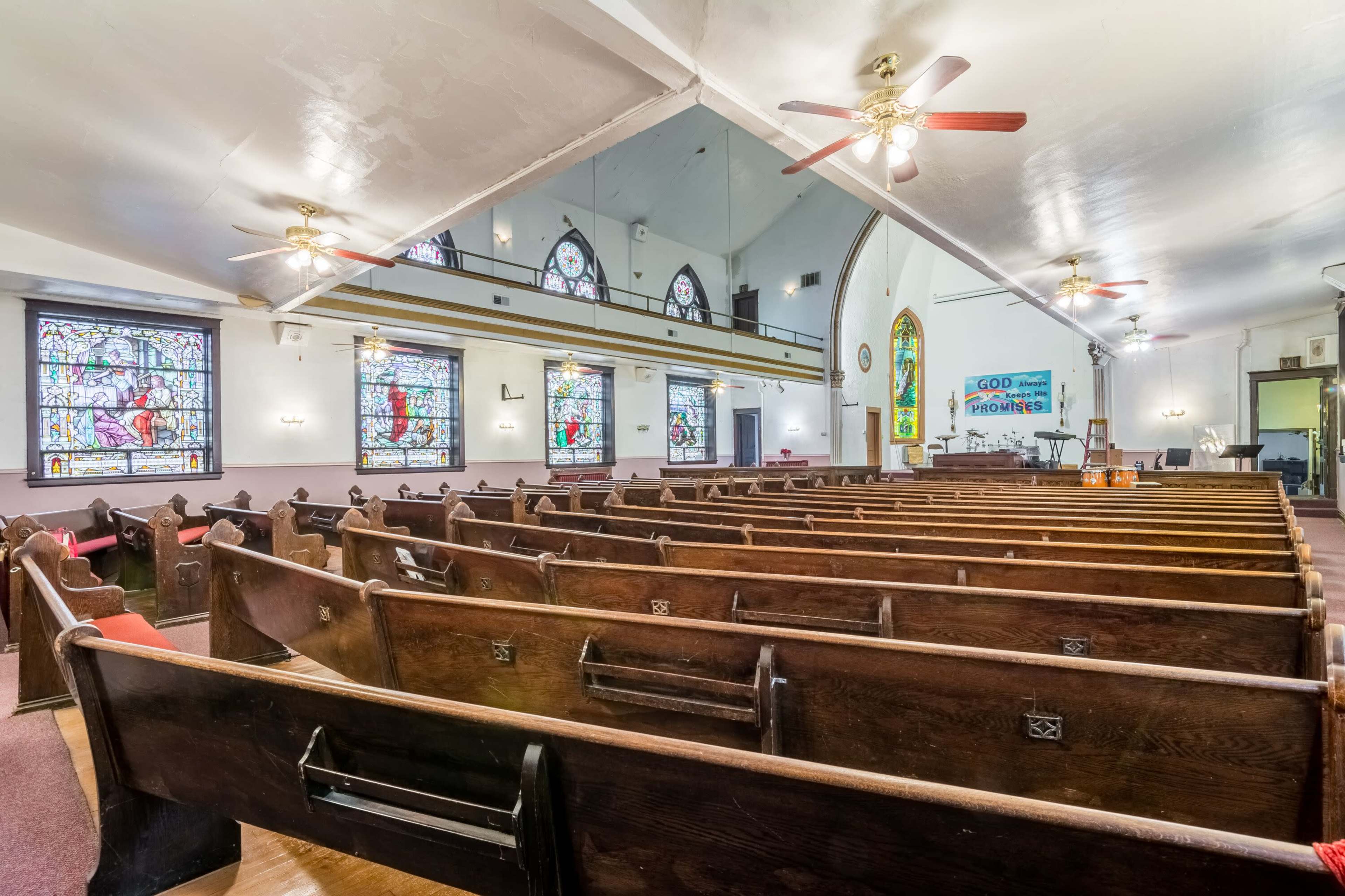 The interior of a church with wooden pews facing stained glass windows and a raised platform at the front.
