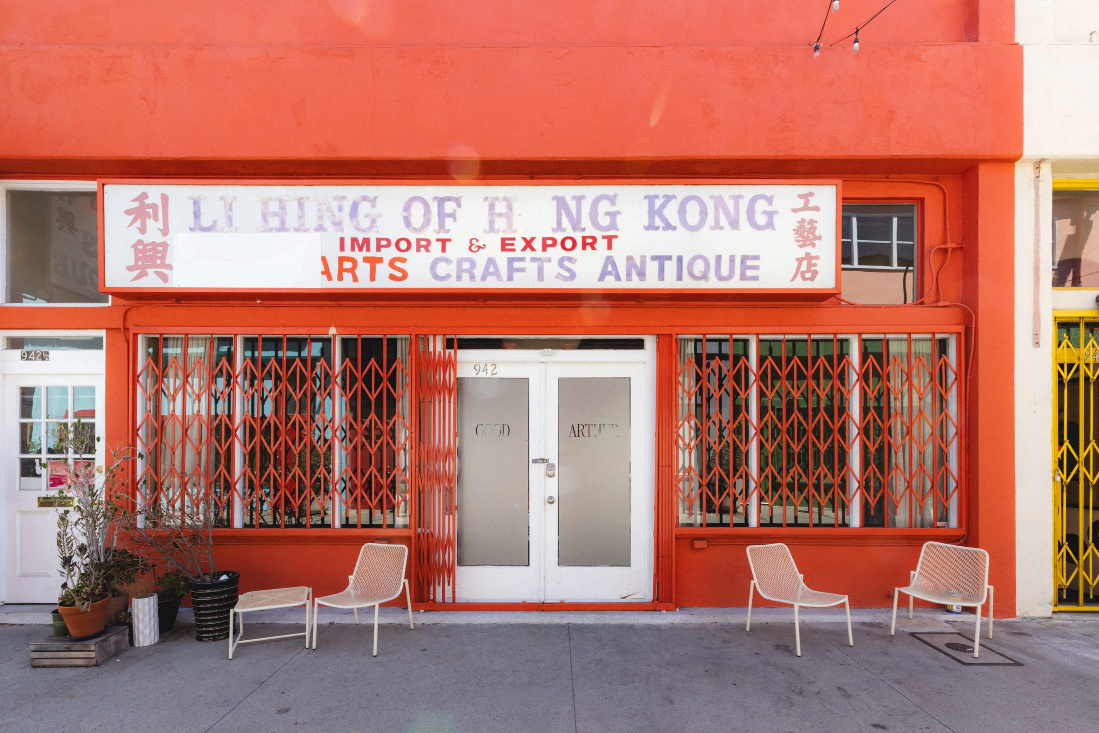 The exterior of a bright red storefront features a sign that reads "Li Hing of Hong Kong Import & Export Arts Crafts Antique," with white glass doors and metal security grates.