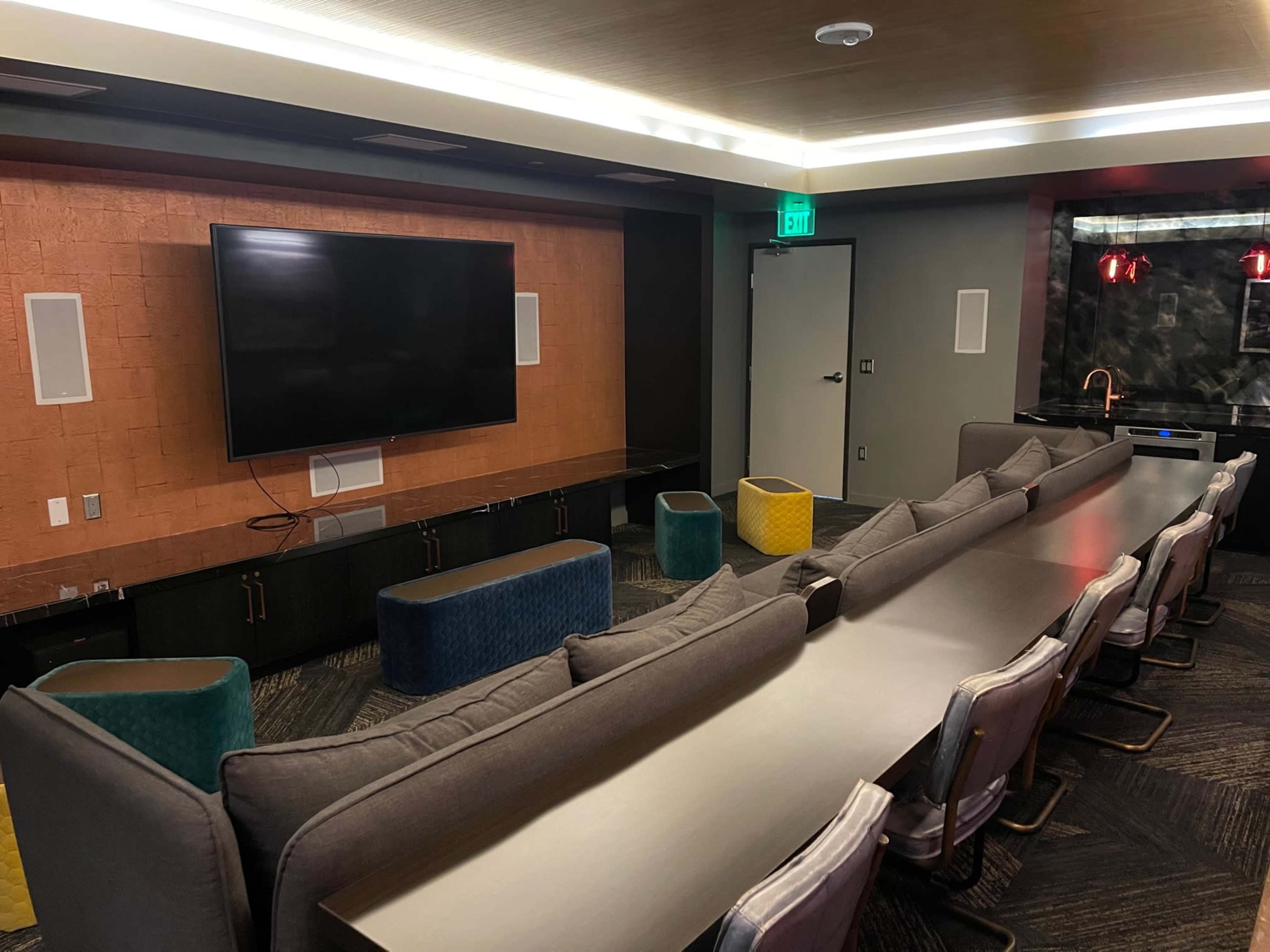 A modern conference room features a large TV mounted on a wall with a long table and seating arranged in front.