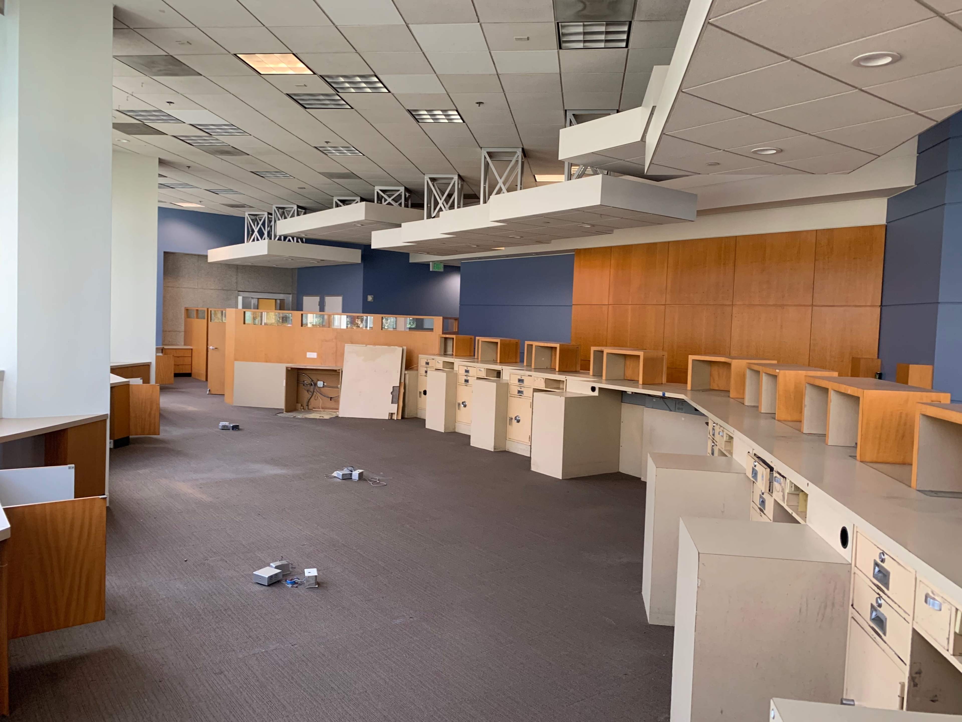The image shows a spacious, empty office interior with desks and cubicle partitions arranged along the walls and debris scattered on the floor.