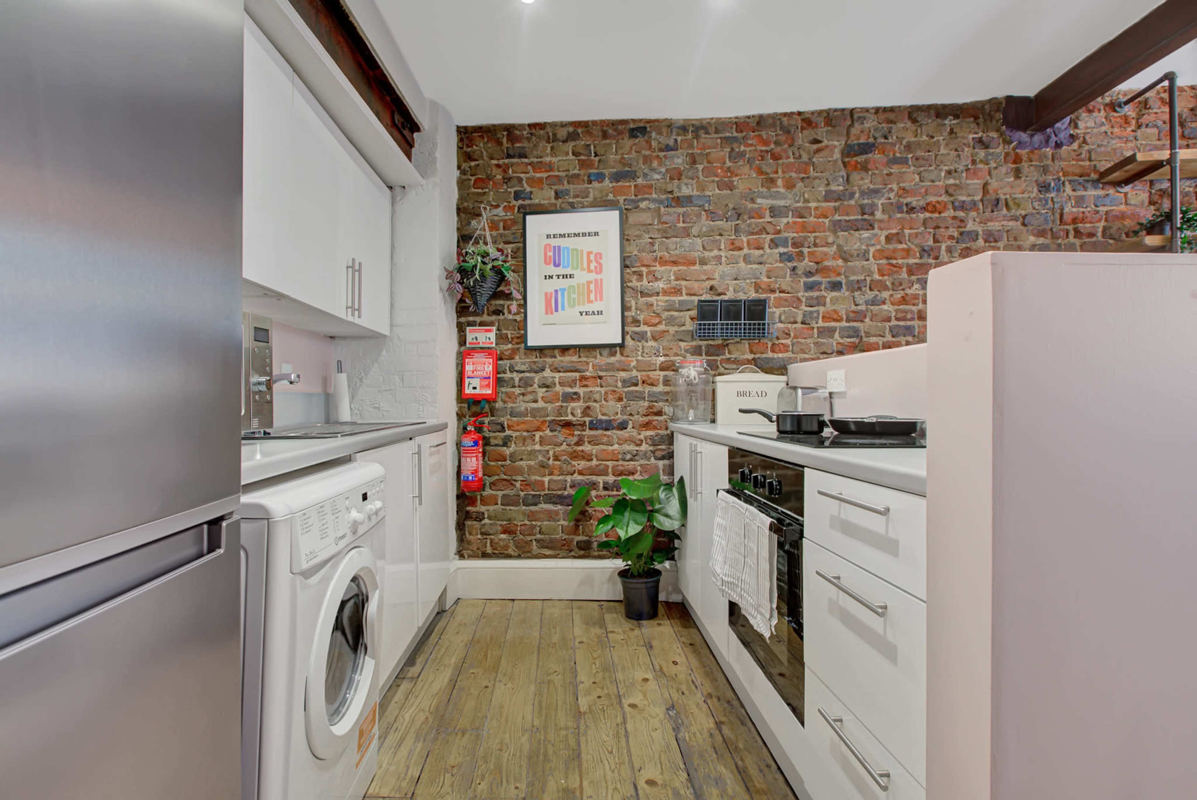 A modern laundry room with white cabinetry, stainless steel appliances, and a brick wall backdrop.