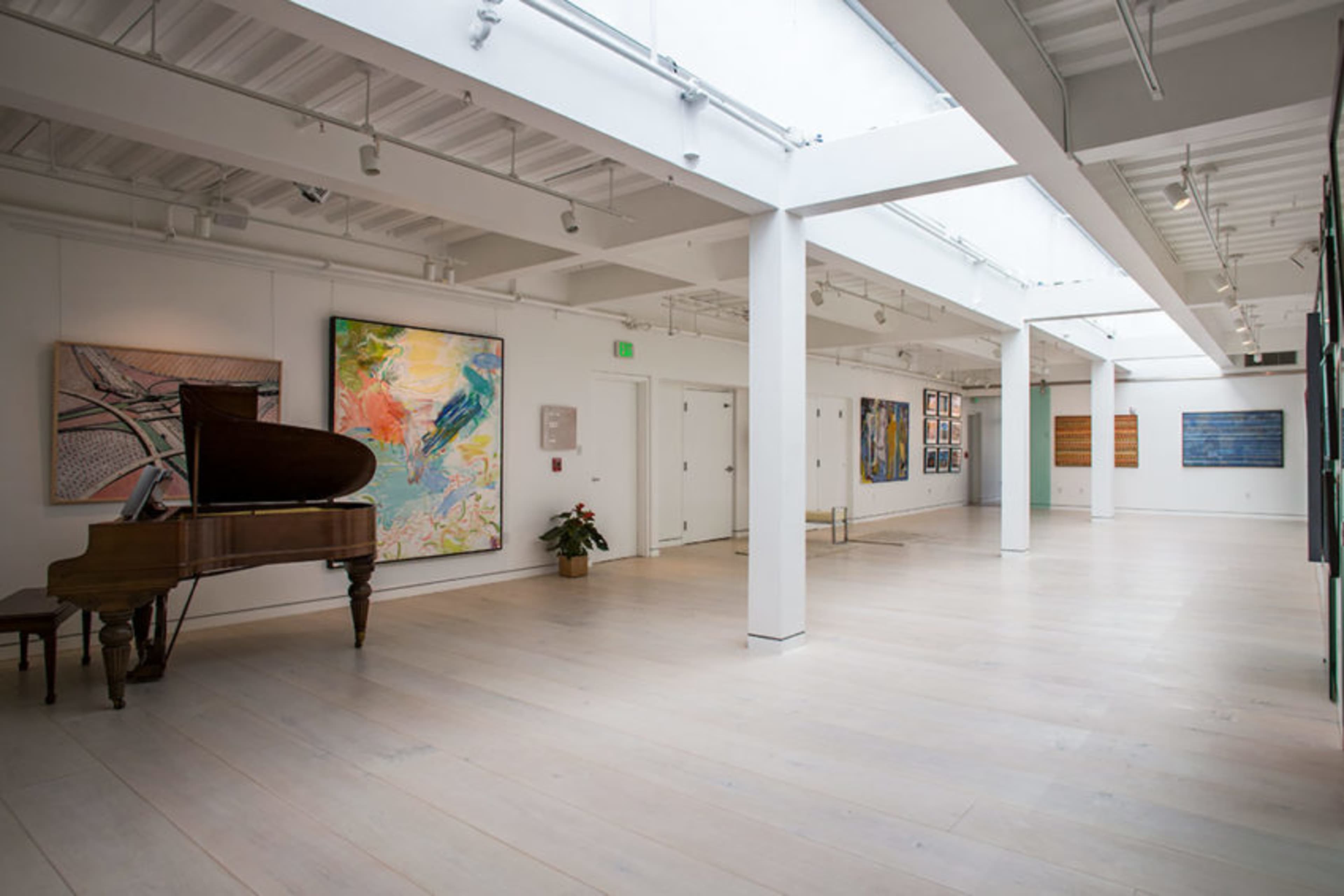 A brightly lit art gallery featuring various paintings on the walls and a grand piano in the corner.