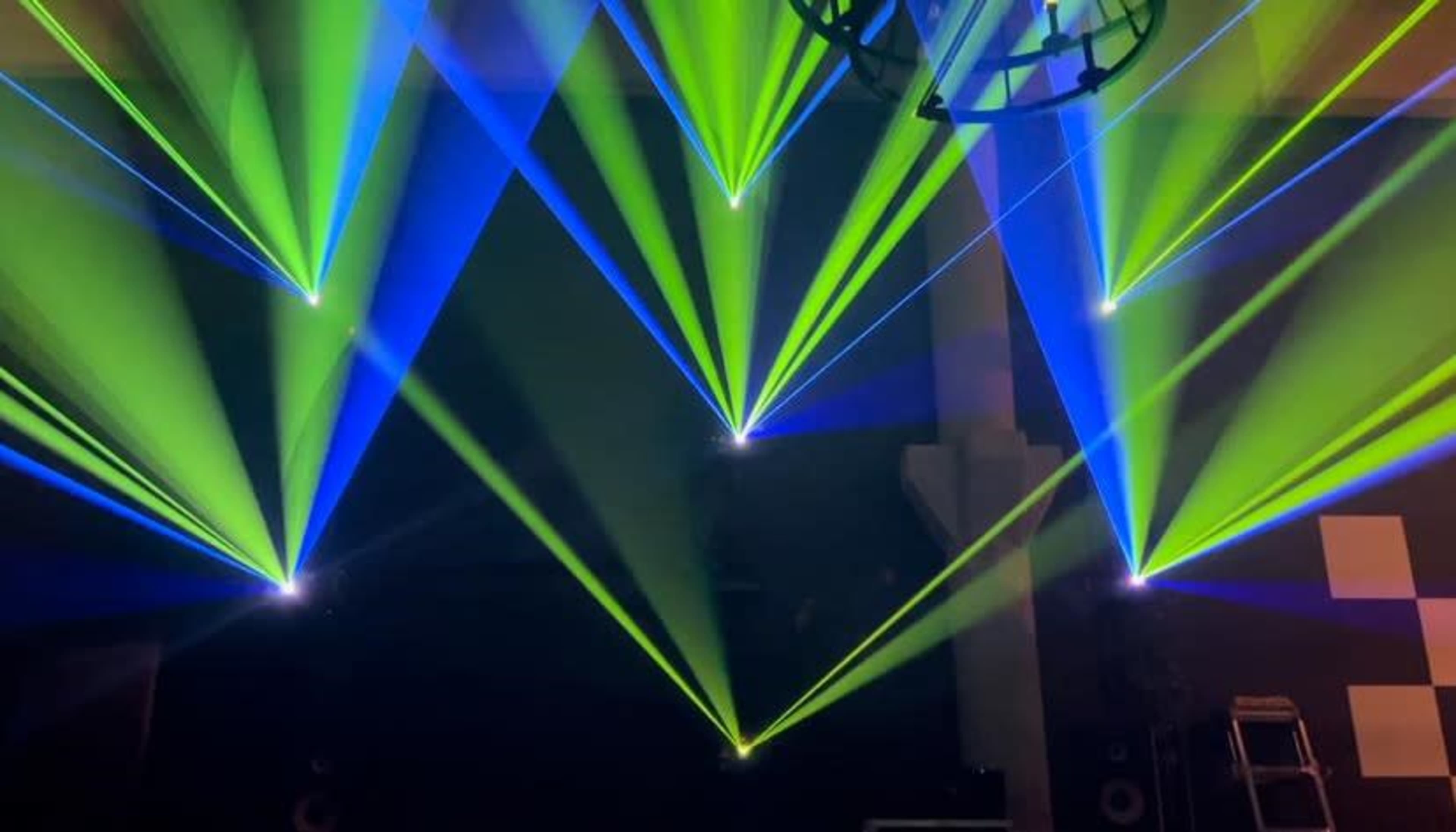 A vibrant display of green and blue laser lights intersecting in a dark venue.