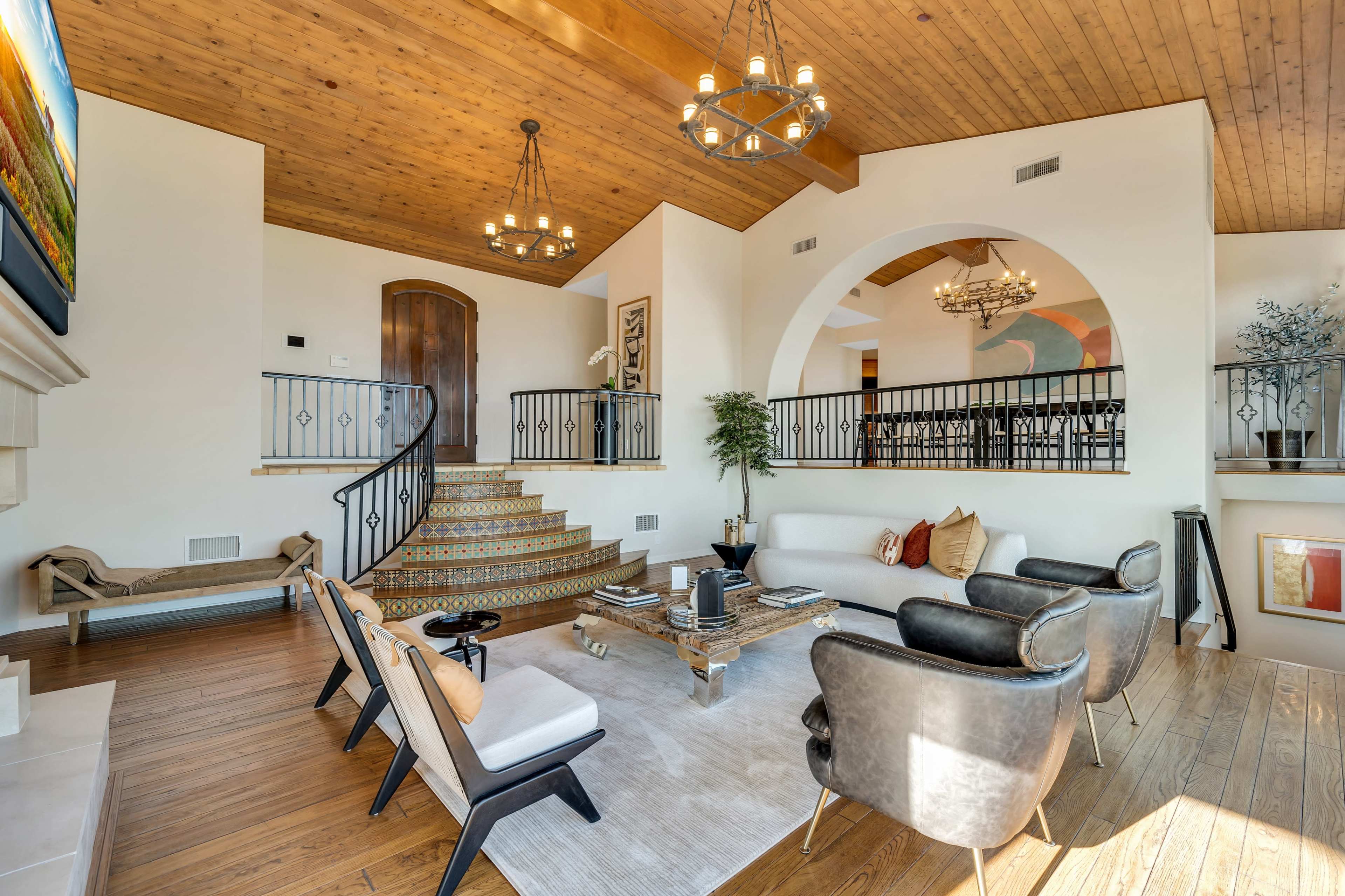 The image shows a spacious living room with a staircase leading to an upper level, featuring a modern seating arrangement and decorative lighting.