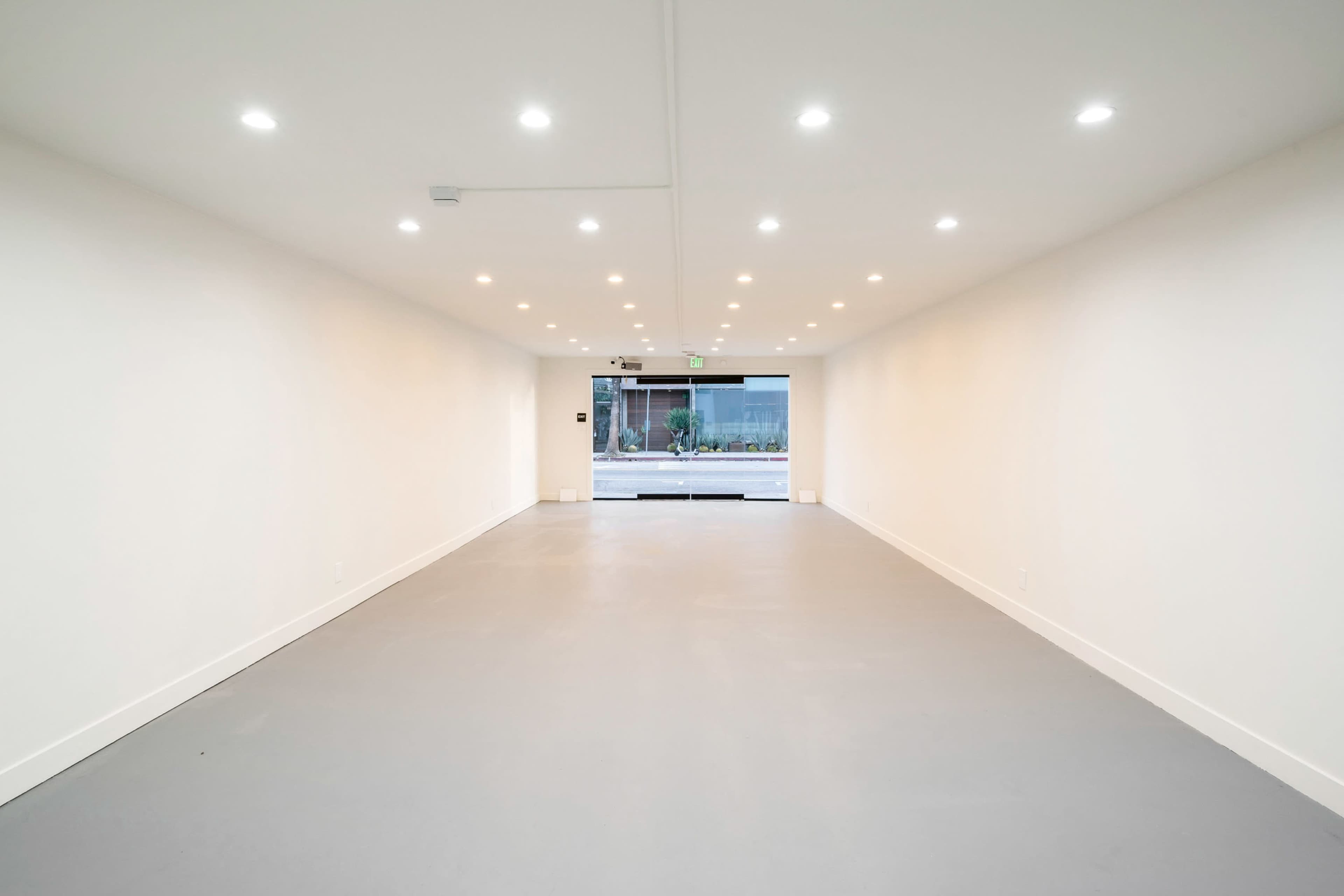 The image shows a spacious, brightly lit interior of a commercial space with a smooth grey floor and an open entrance at the far end.