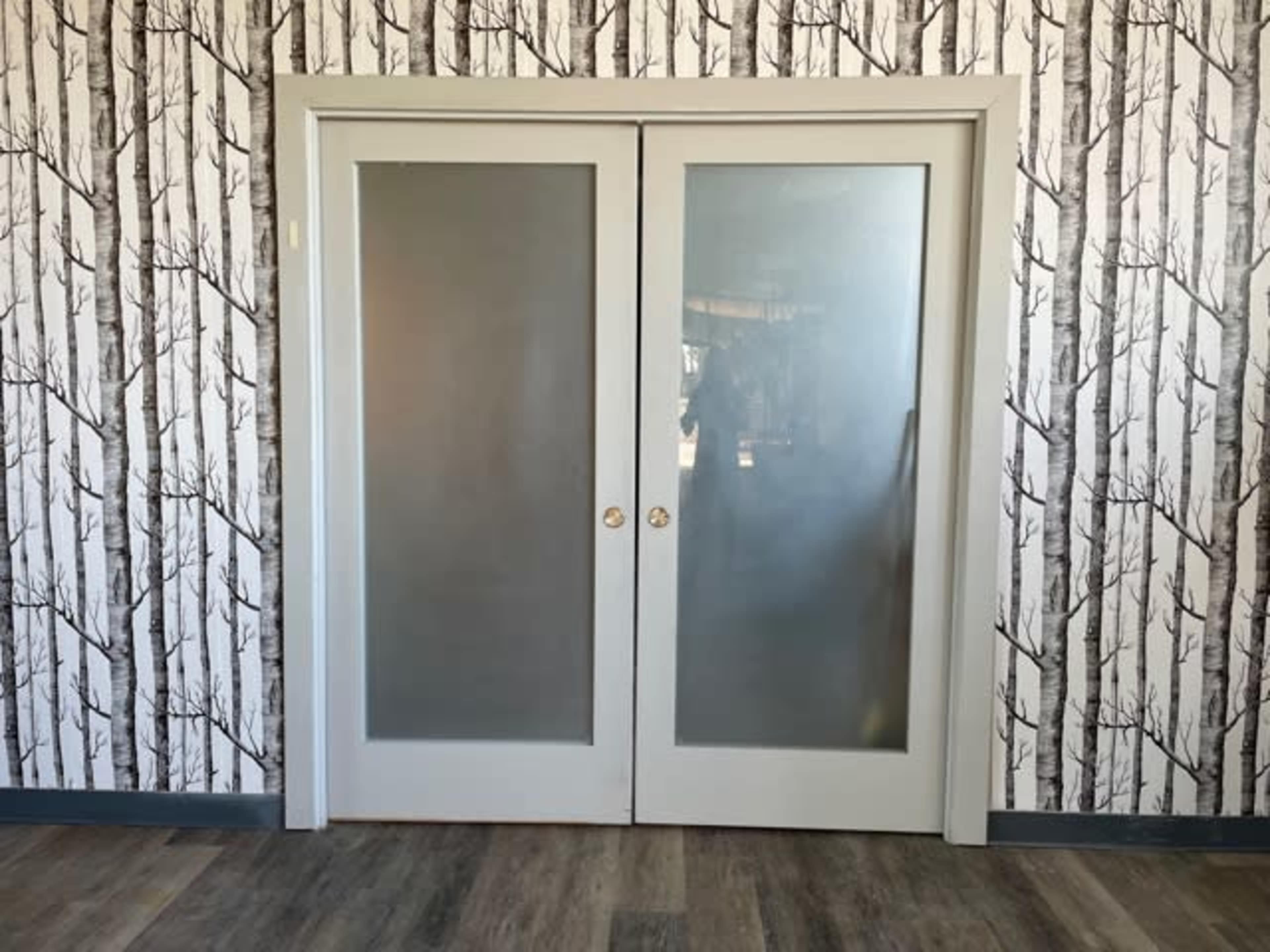A set of double doors with frosted glass panels is framed by a wall adorned with a black and white tree-patterned wallpaper.