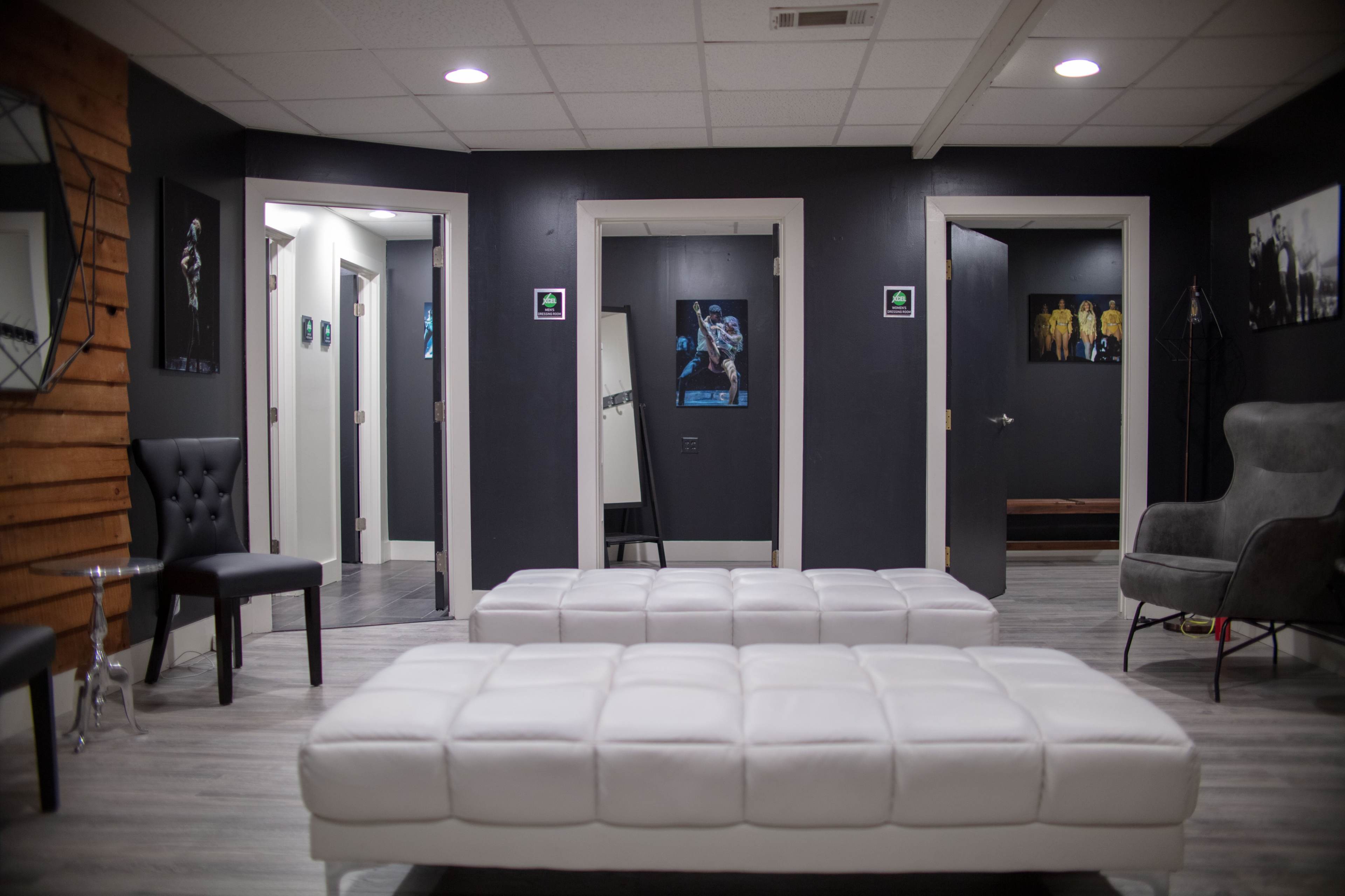 A modern, minimalist waiting area with white benches, black walls, and several doors leading to other rooms.