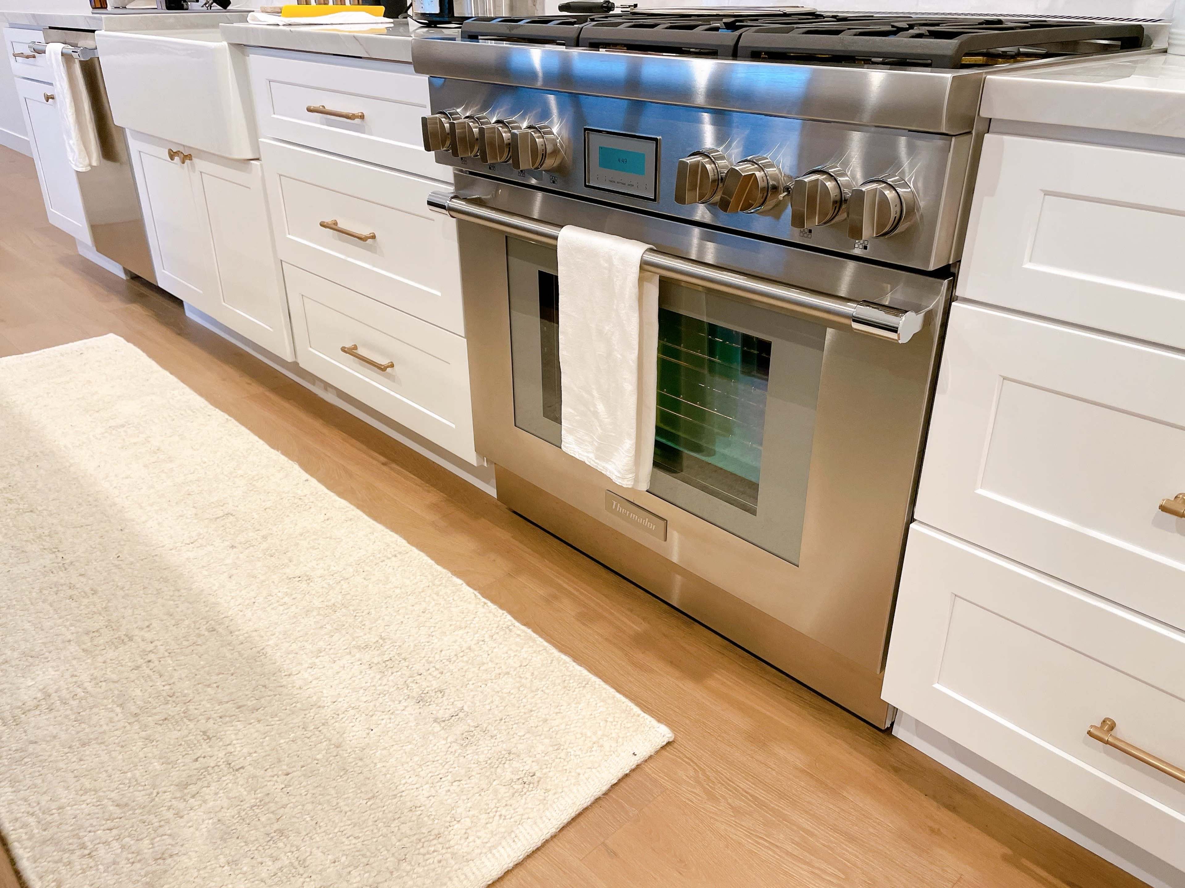 A stainless steel oven installed in a kitchen with white cabinets and a light-colored rug on the floor.
