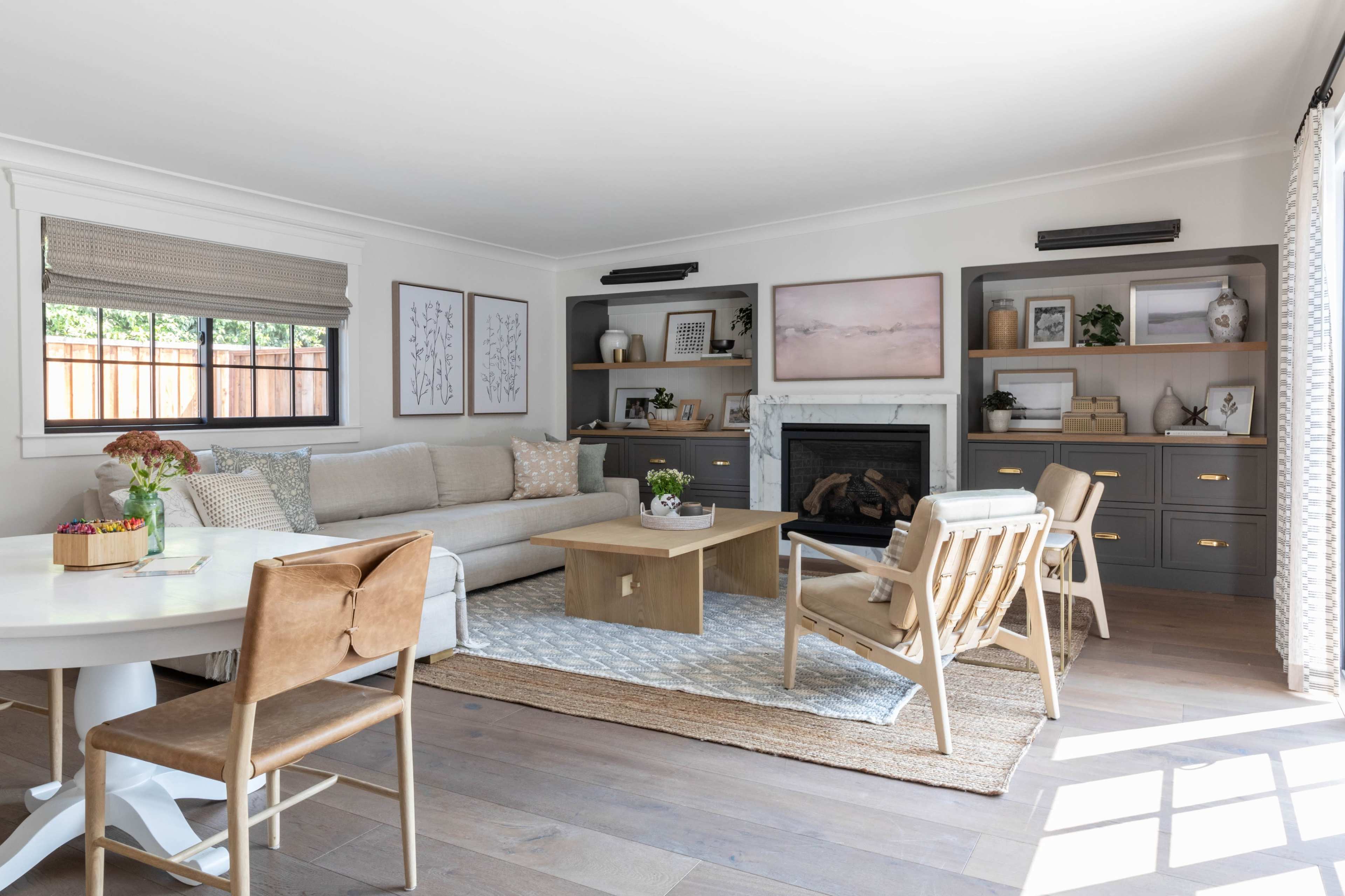 A modern living room with a beige sofa, a wooden coffee table, and light-colored chairs arranged around a rug, complemented by built-in shelves and a fireplace.