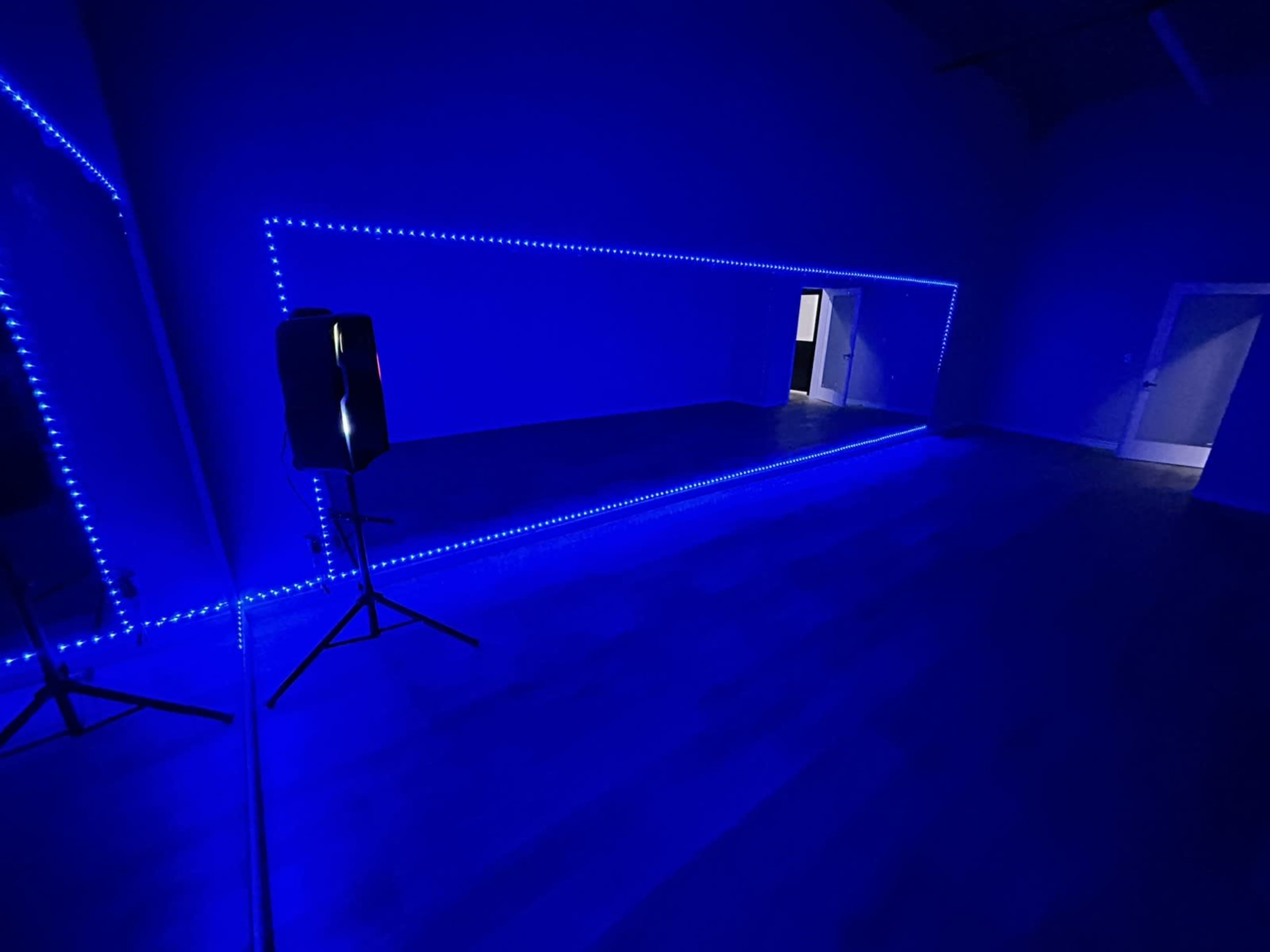 A room with blue LED lights outlining a mirrored wall, featuring a speaker on a stand.
