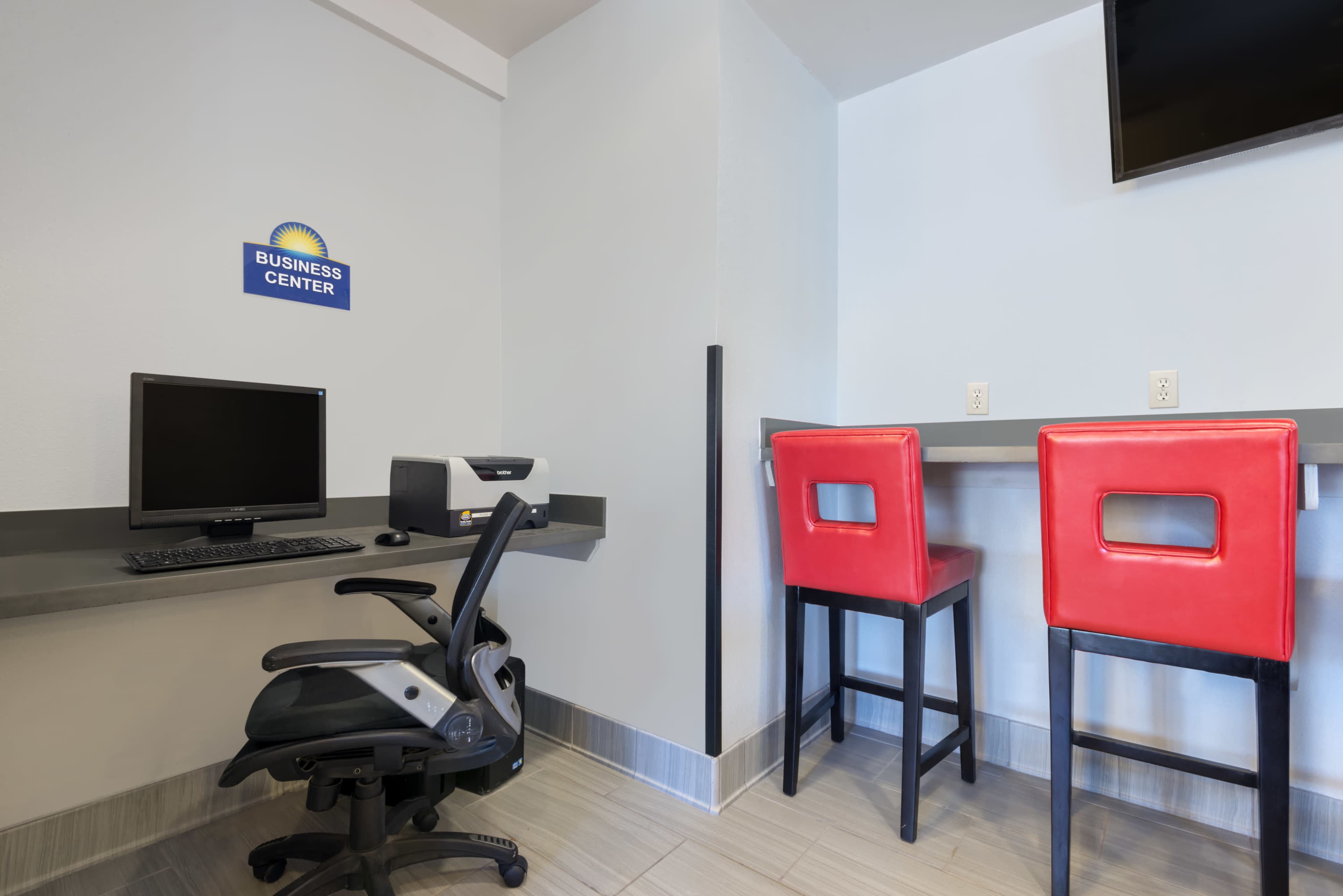 A business center with a computer workstation and two red barstools at a counter.