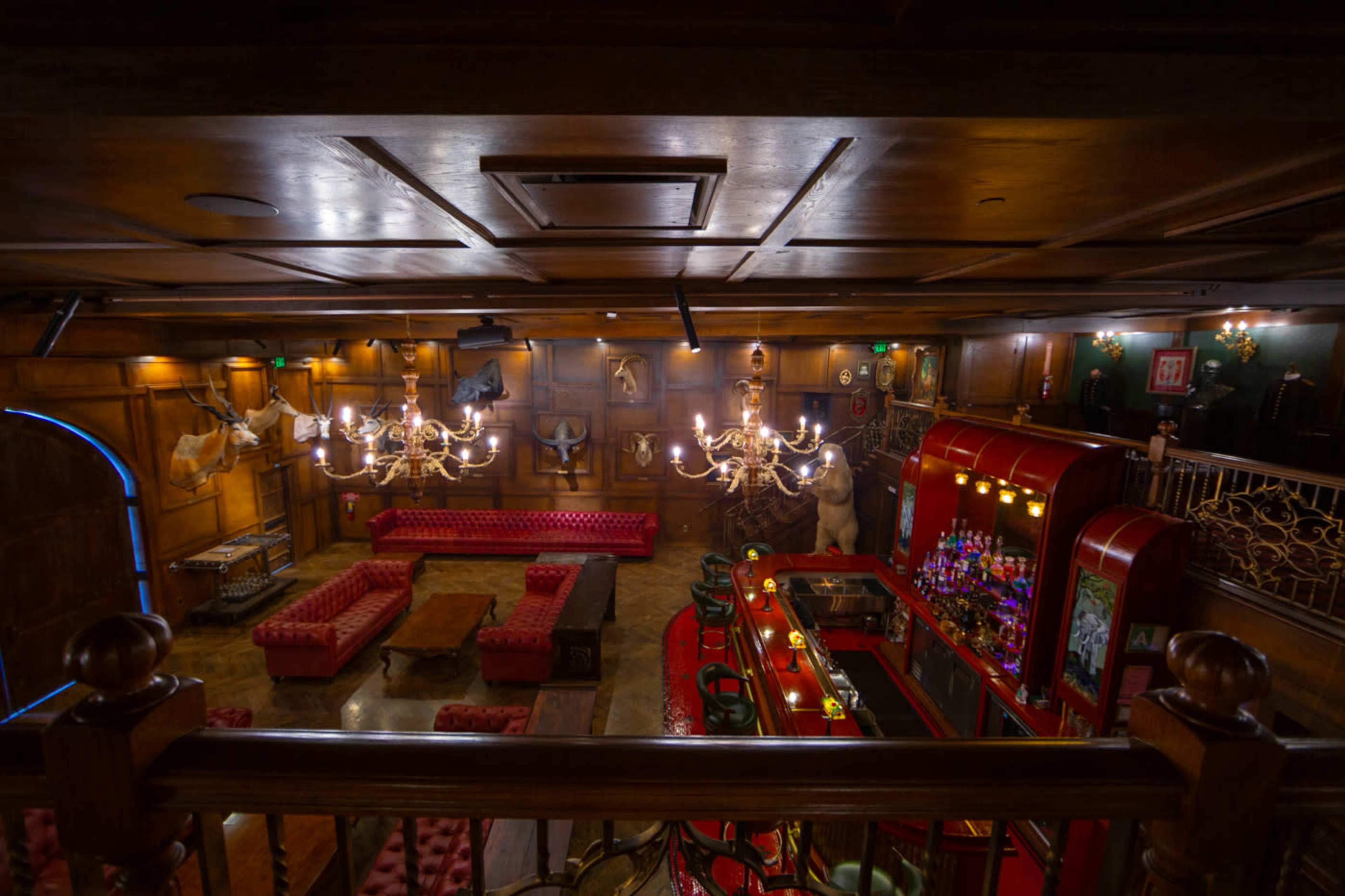 The image shows a dimly lit bar area with red tufted seating, a wooden ceiling, and a decorative bar featuring various bottles.