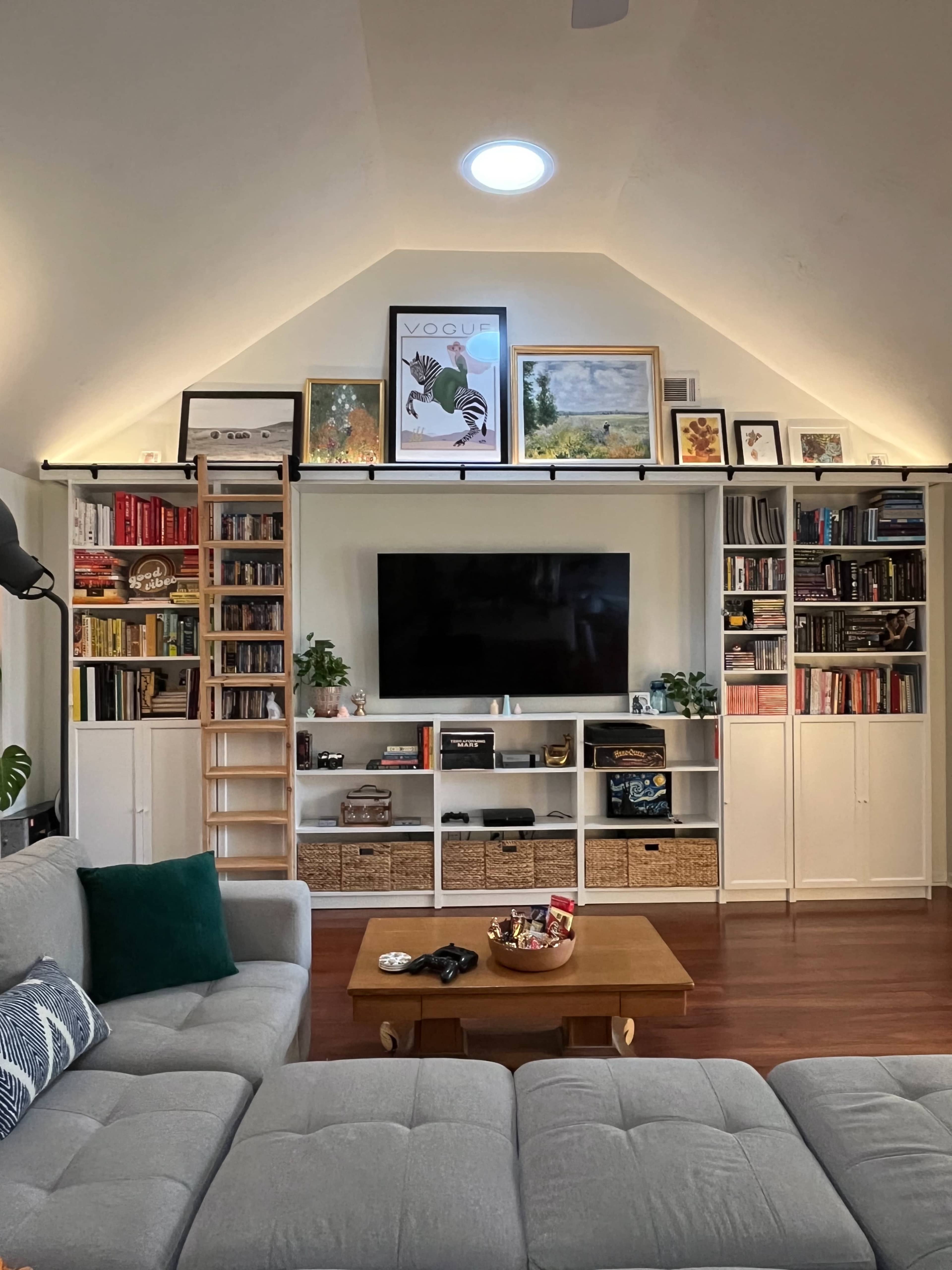 The image shows a cozy living room with a large bookshelf, a flat-screen TV, a coffee table, and a sectional sofa.