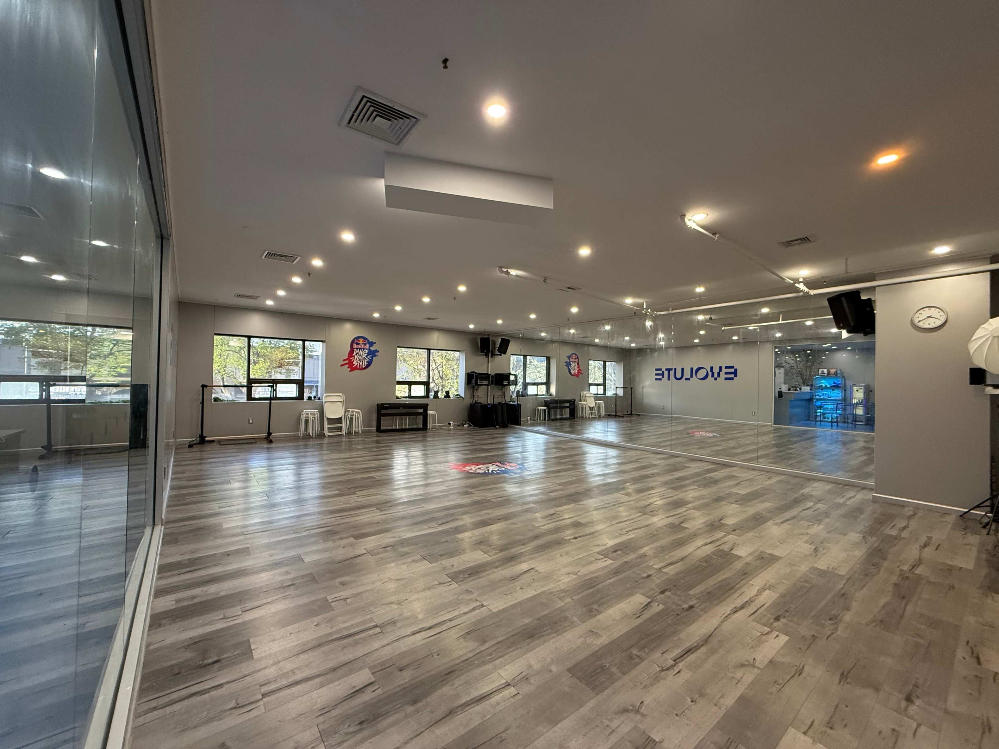 The image shows a spacious, well-lit dance studio with large mirrors, wooden flooring, and a few exercise props in the background.