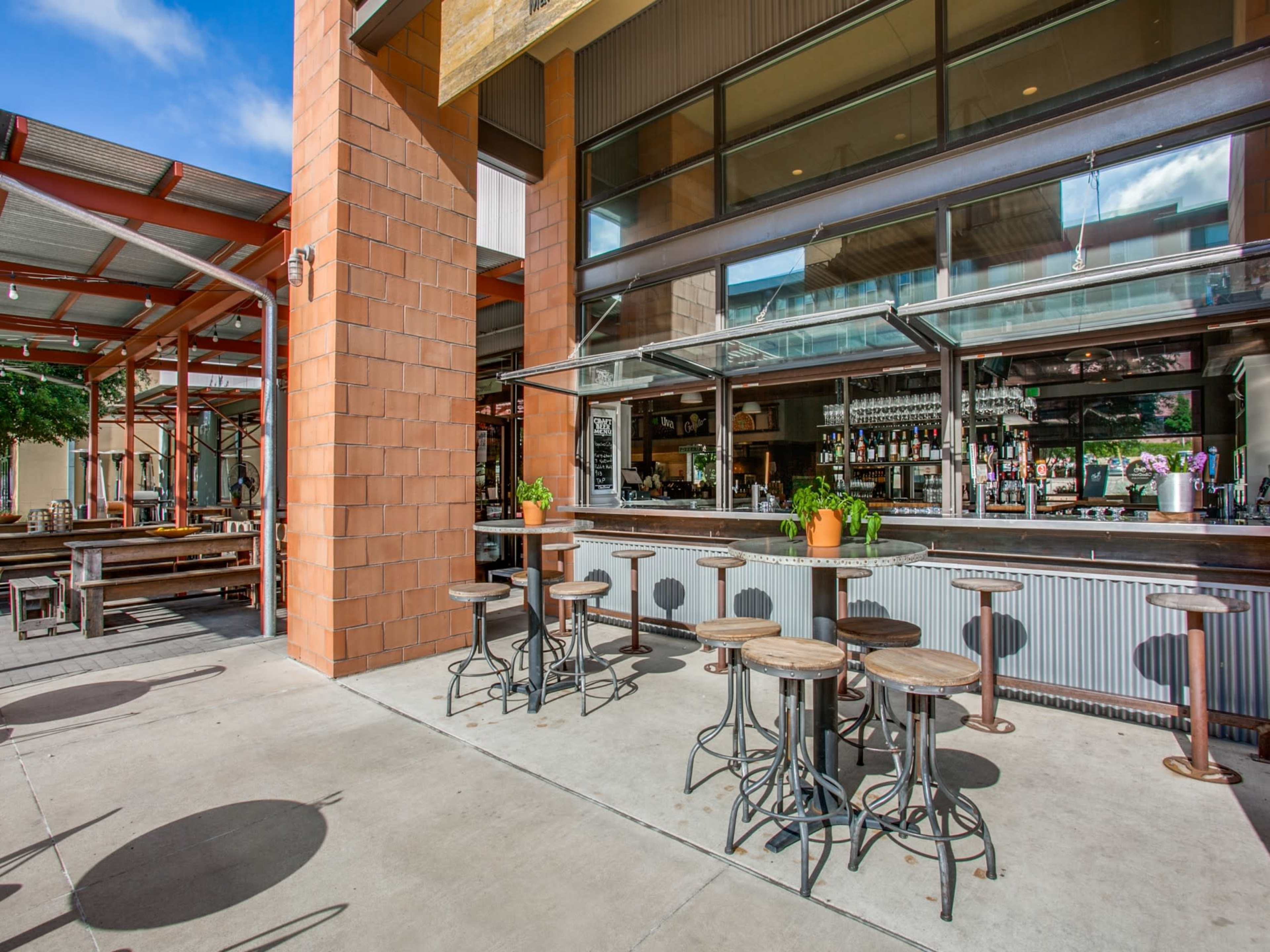 A modern outdoor bar with stools and a spacious seating area under a roofed structure.