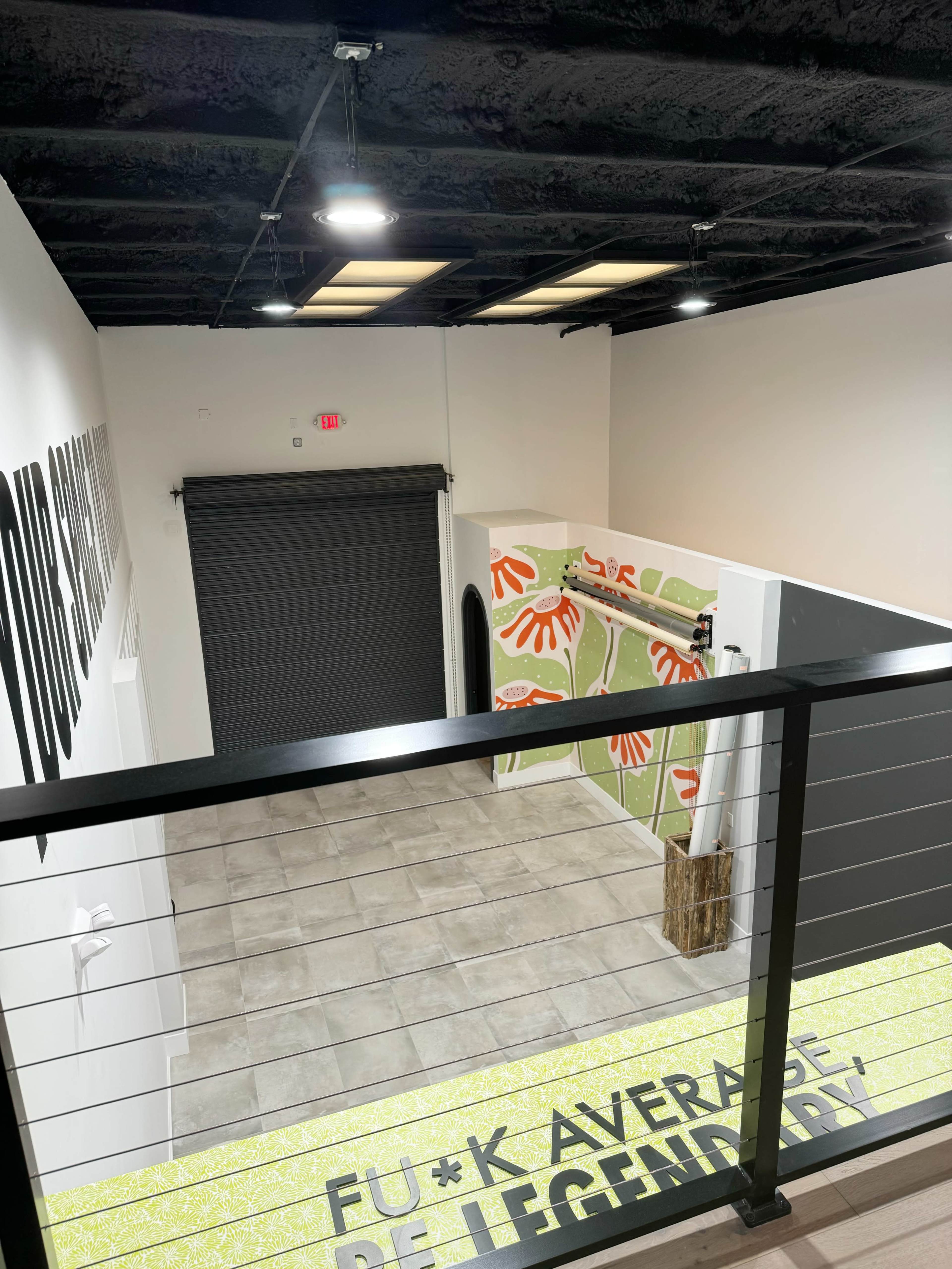 A modern interior space with a view from a balcony, featuring a decorative wall with colorful handprints and a large, closed garage door.