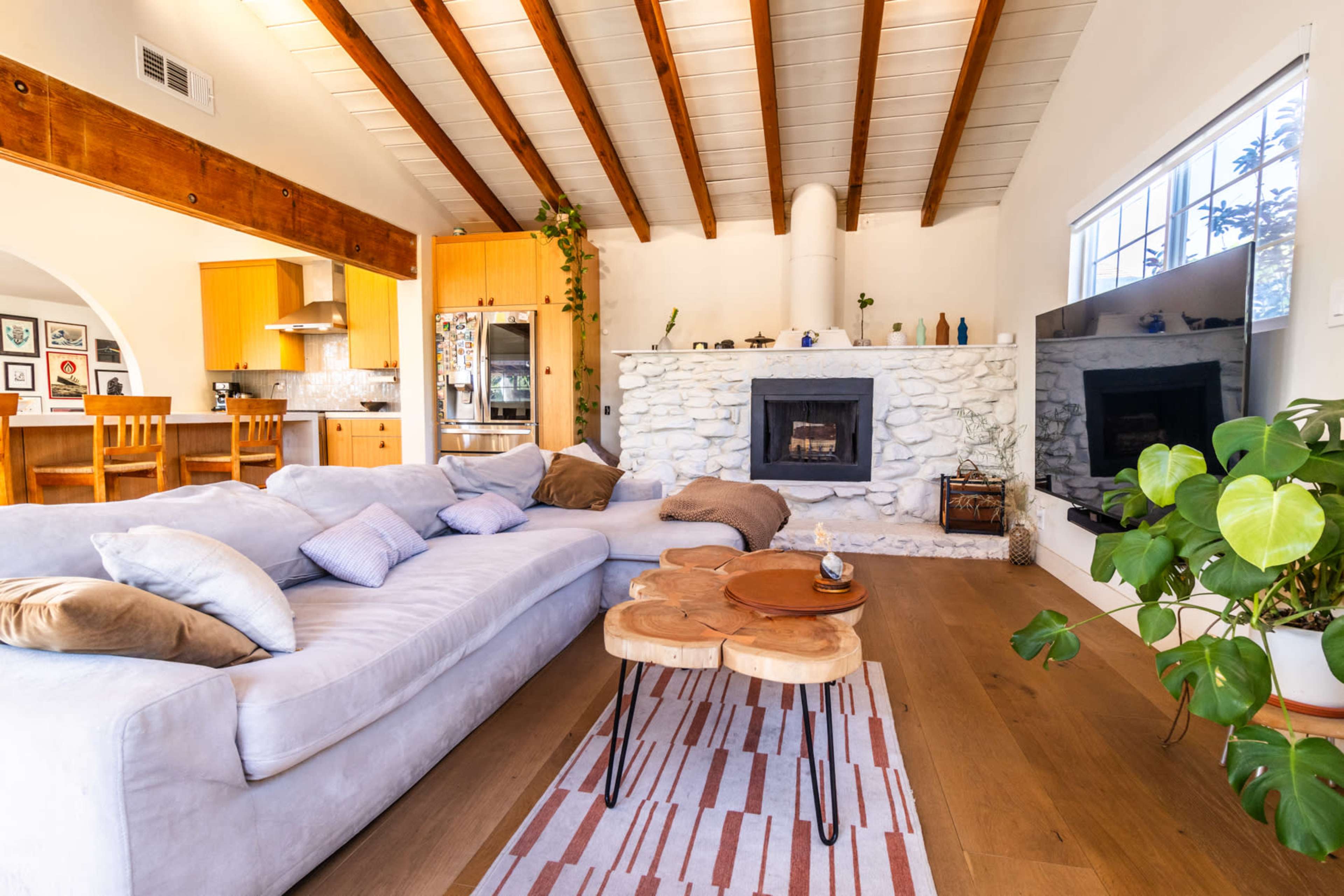 A cozy living room with a stone fireplace, a large sectional couch, and a wooden coffee table, featuring an open layout that connects to a kitchen area.