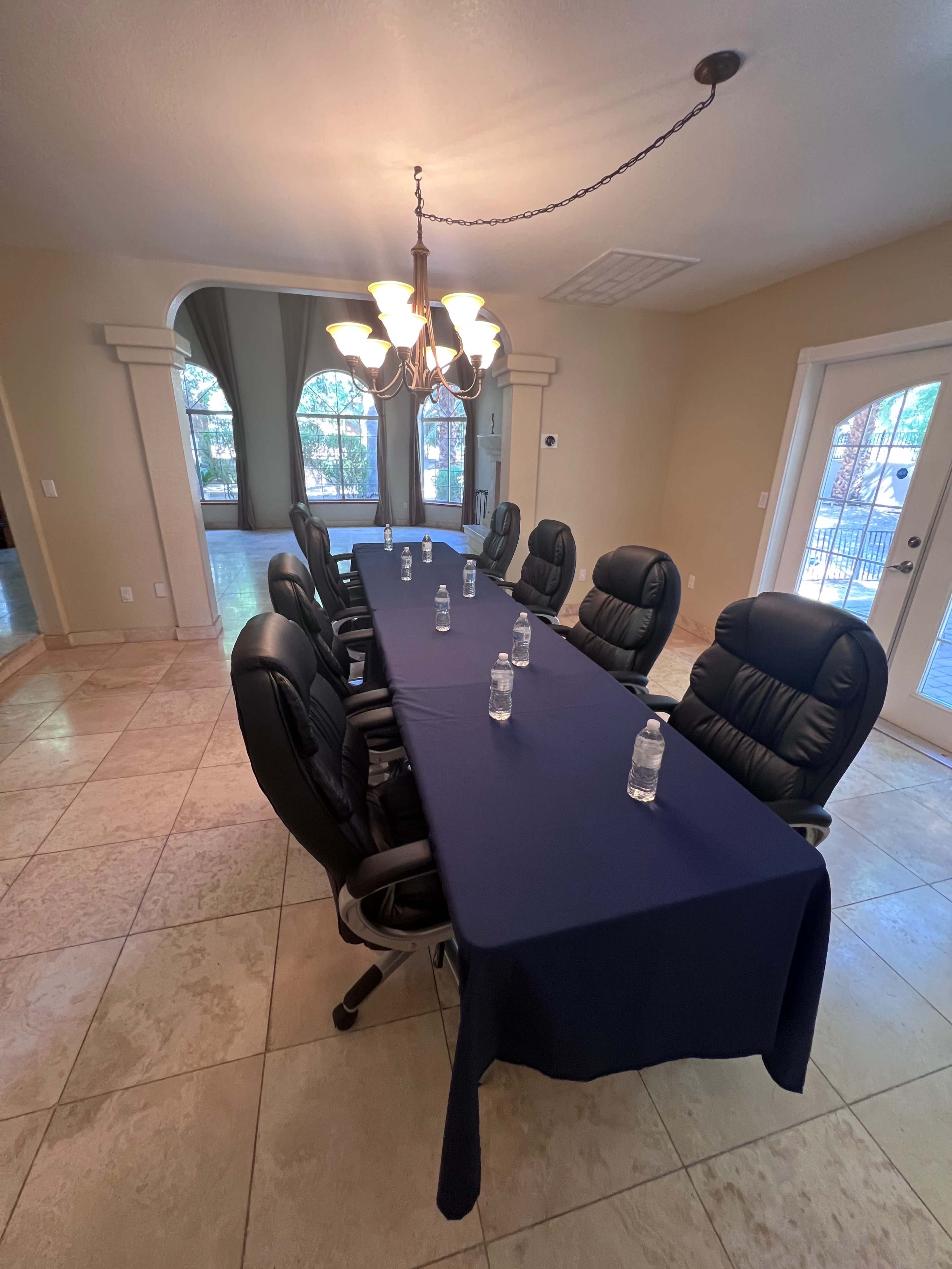 A long conference table with black chairs and water bottles is set up in a well-lit room.