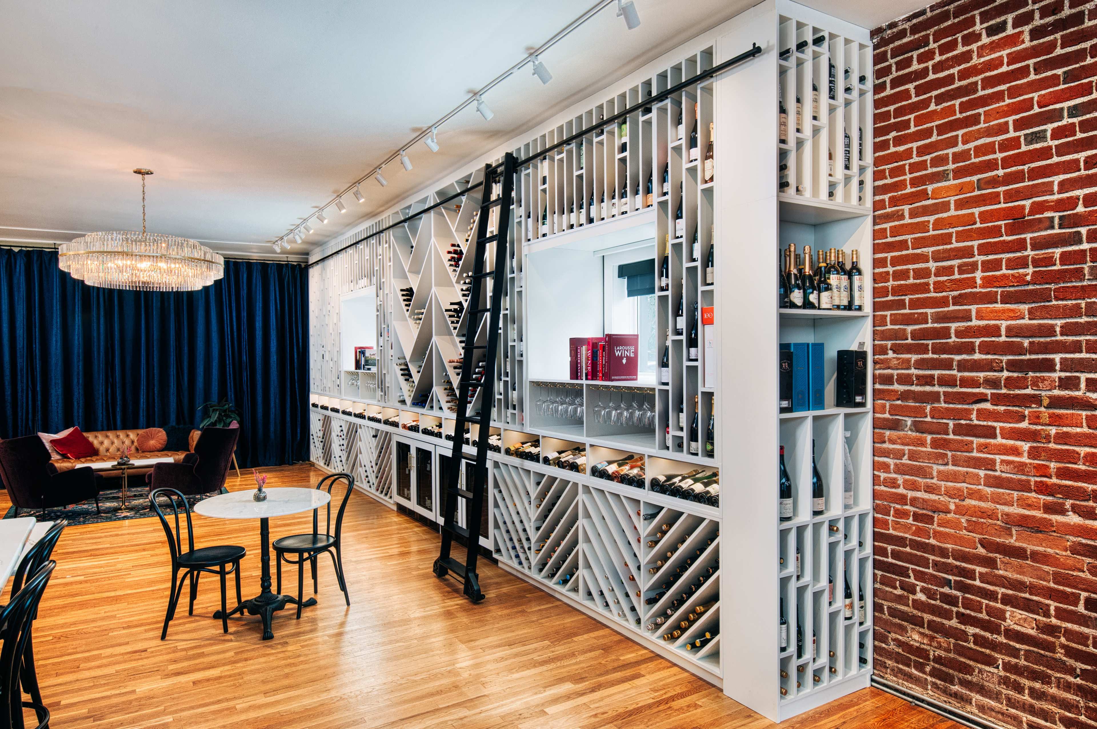 A modern interior features a wine storage wall with a ladder, surrounded by a seating area and brick accent wall.