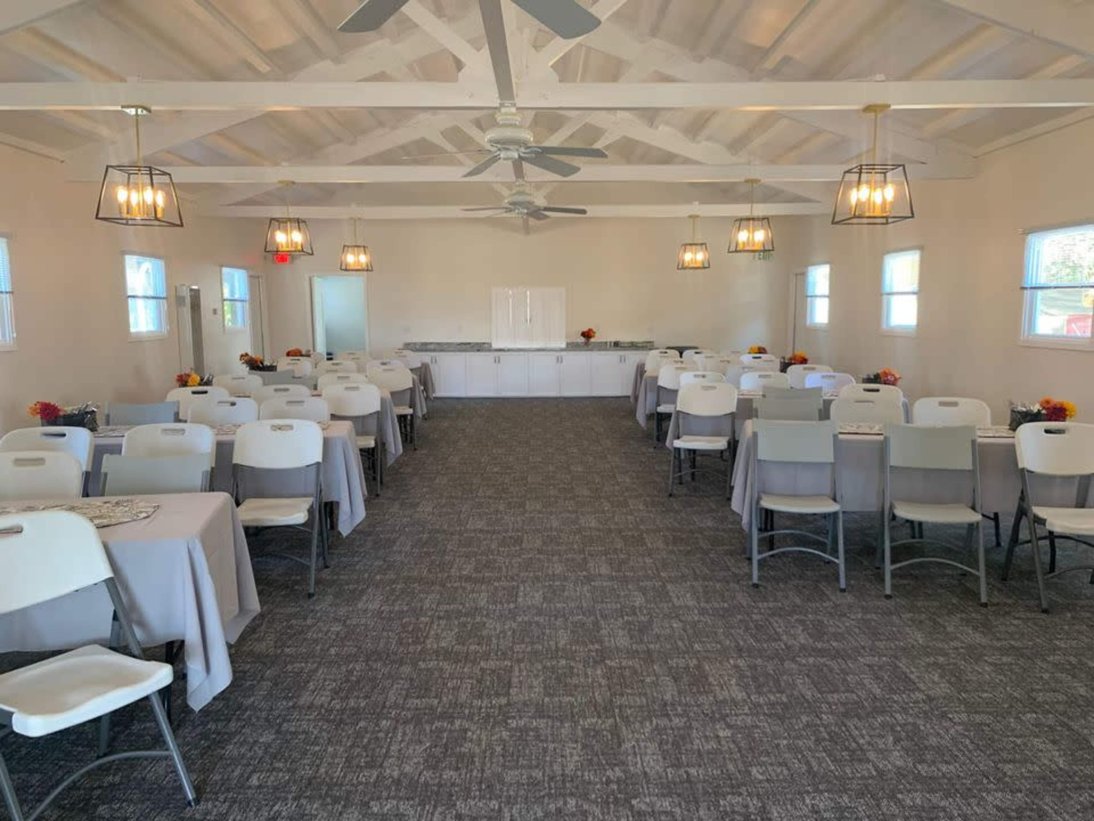 A spacious indoor venue features rows of tables covered with gray tablecloths, arranged facing a serving area with cabinets.