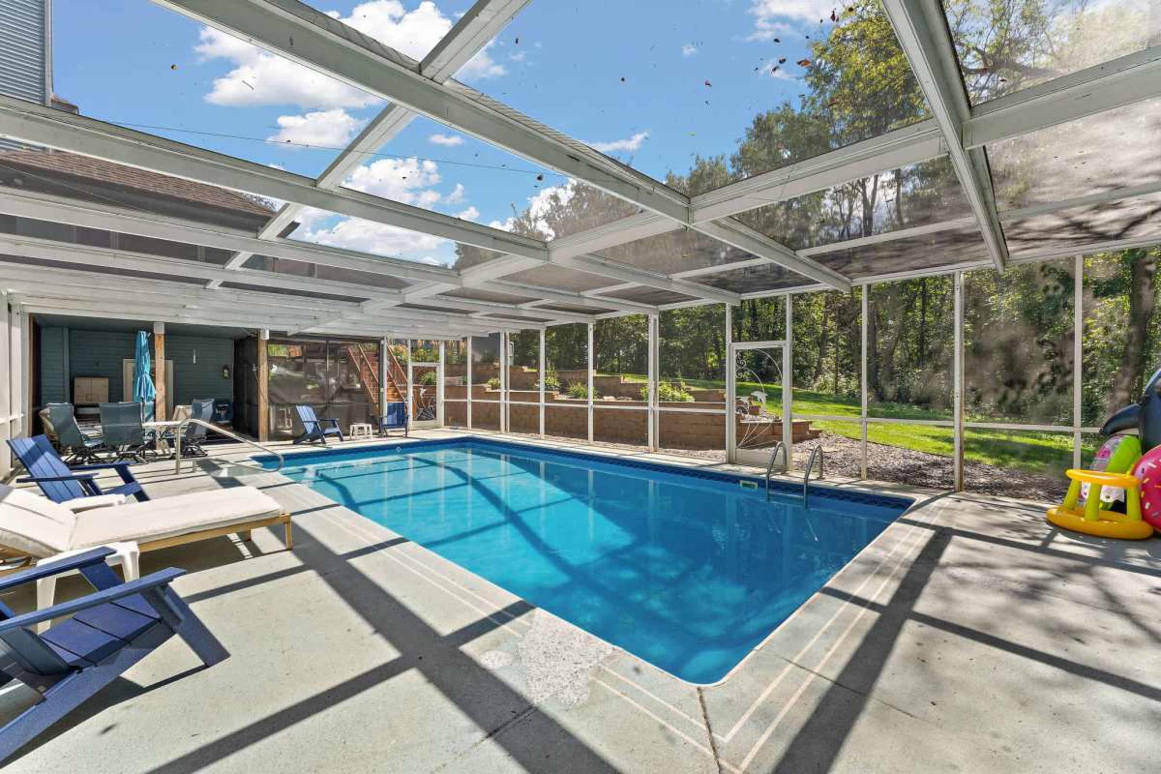 The image shows a screened-in pool area with a clear blue swimming pool, lounge chairs nearby, and a grassy backyard in the background.