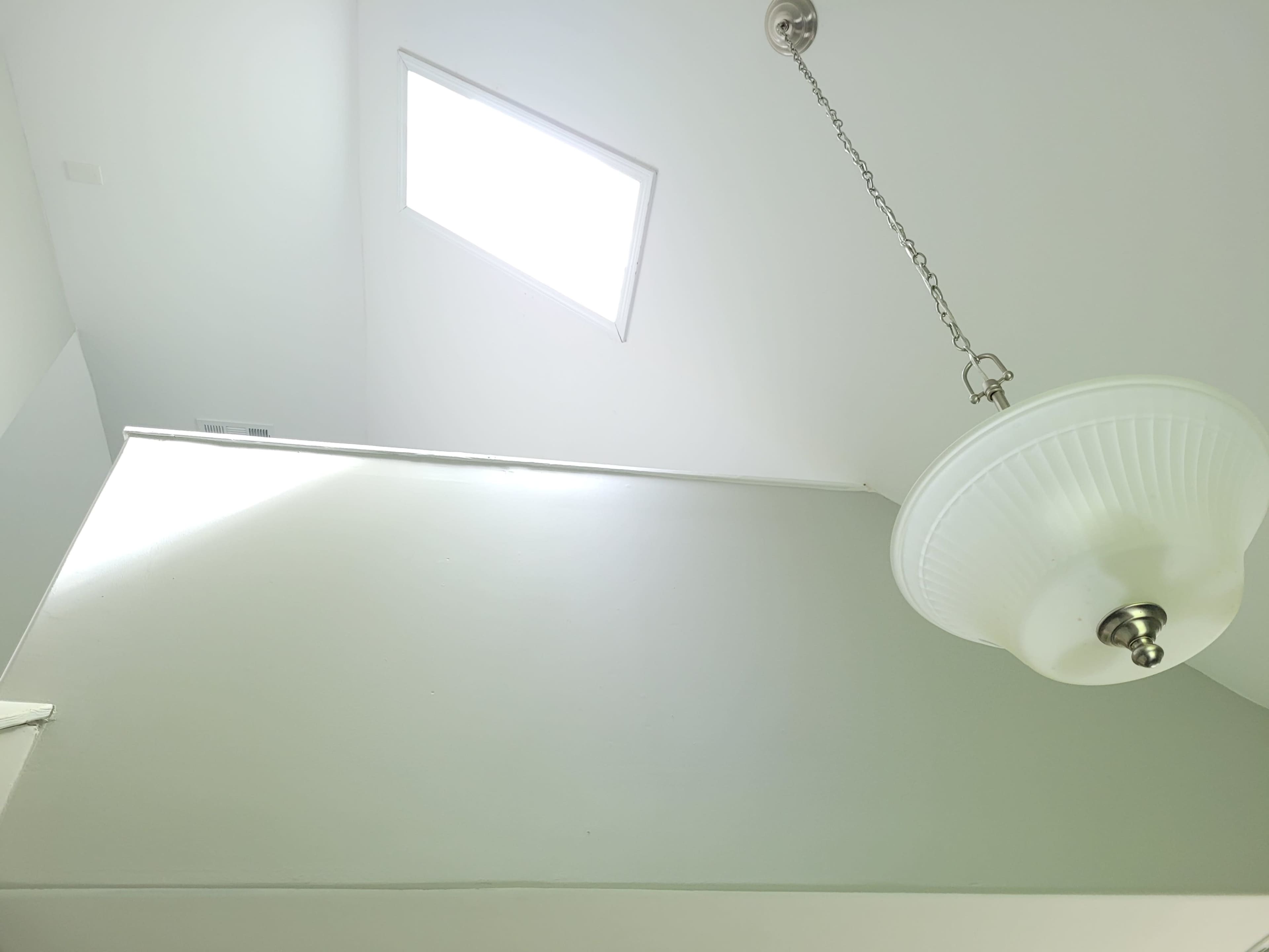 A low-angle view of a white ceiling with a skylight and a hanging light fixture.