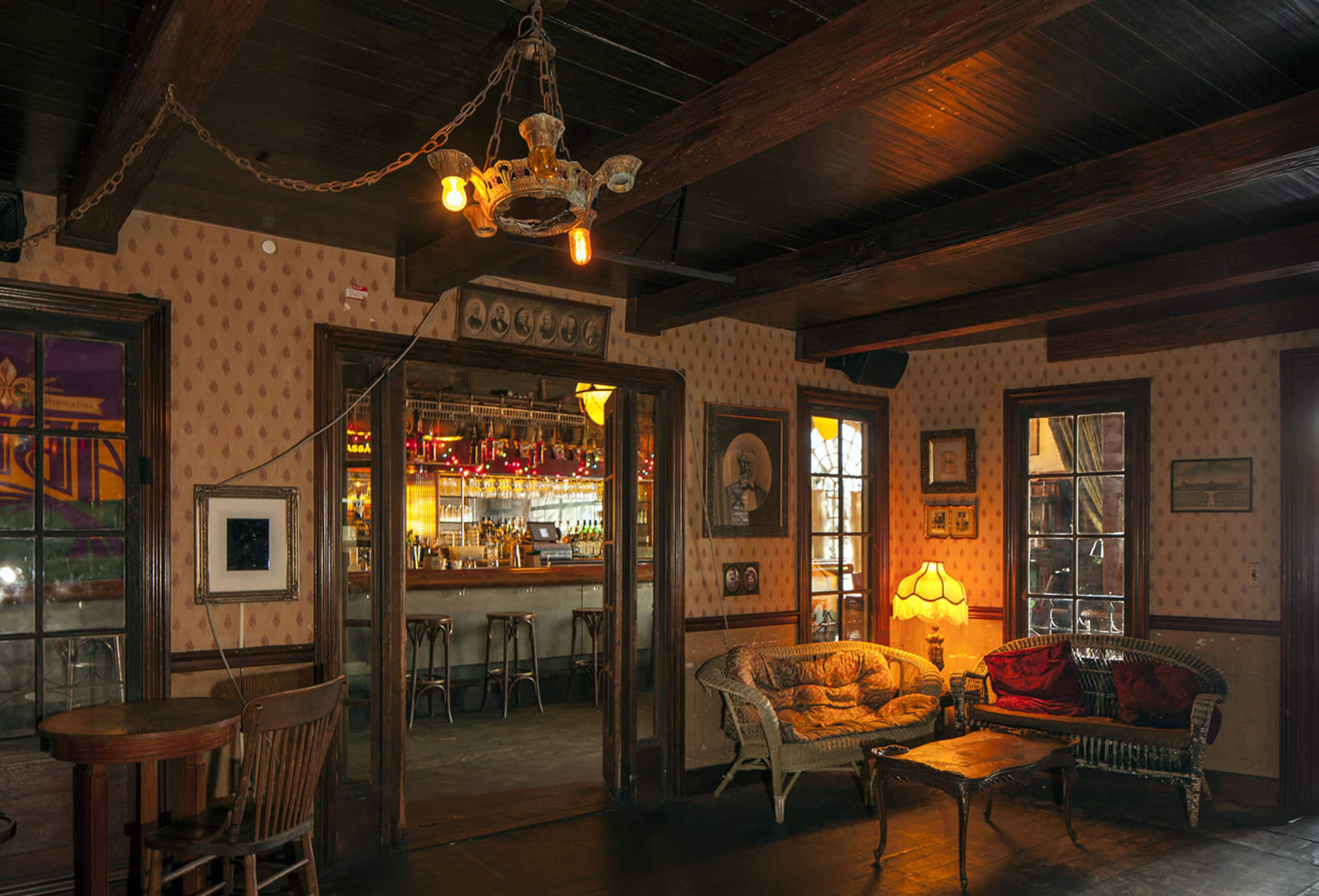 A cozy interior features vintage furniture, warm lighting, and a bar area visible through an open doorway.