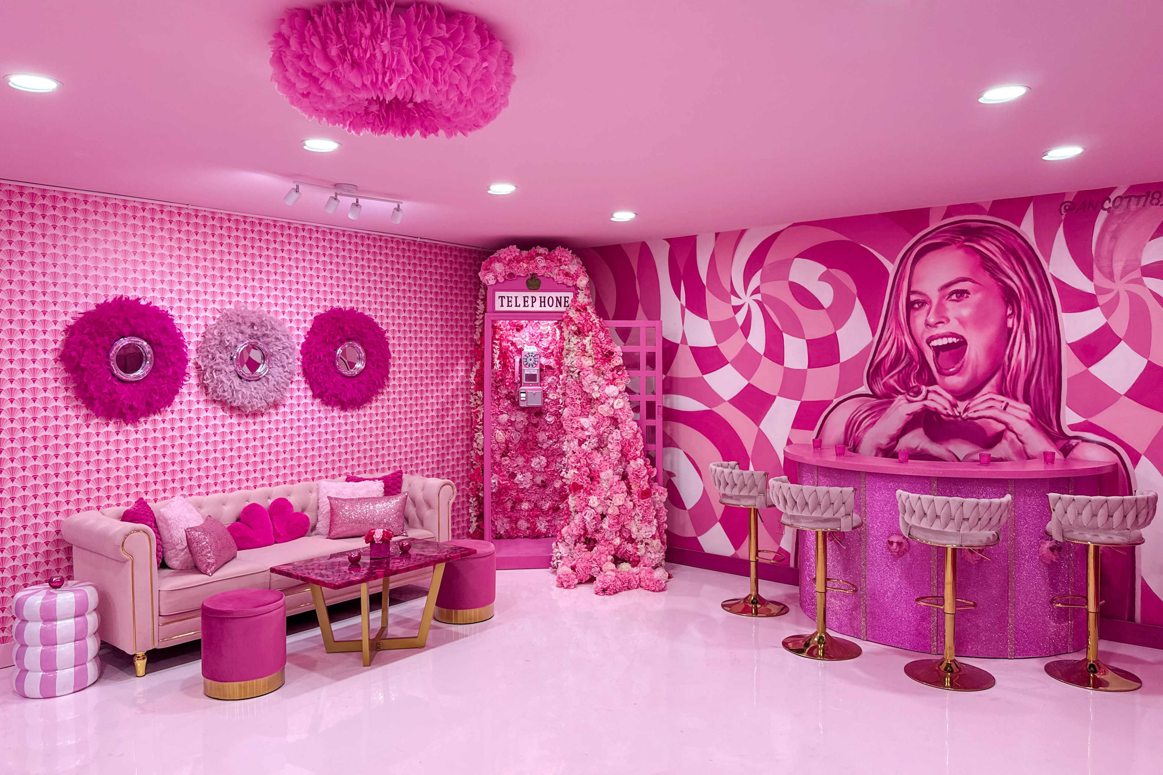 The image shows a vibrant pink room featuring a sofa, bar, and a decorated wall, all embellished with various shades of pink and floral decorations.