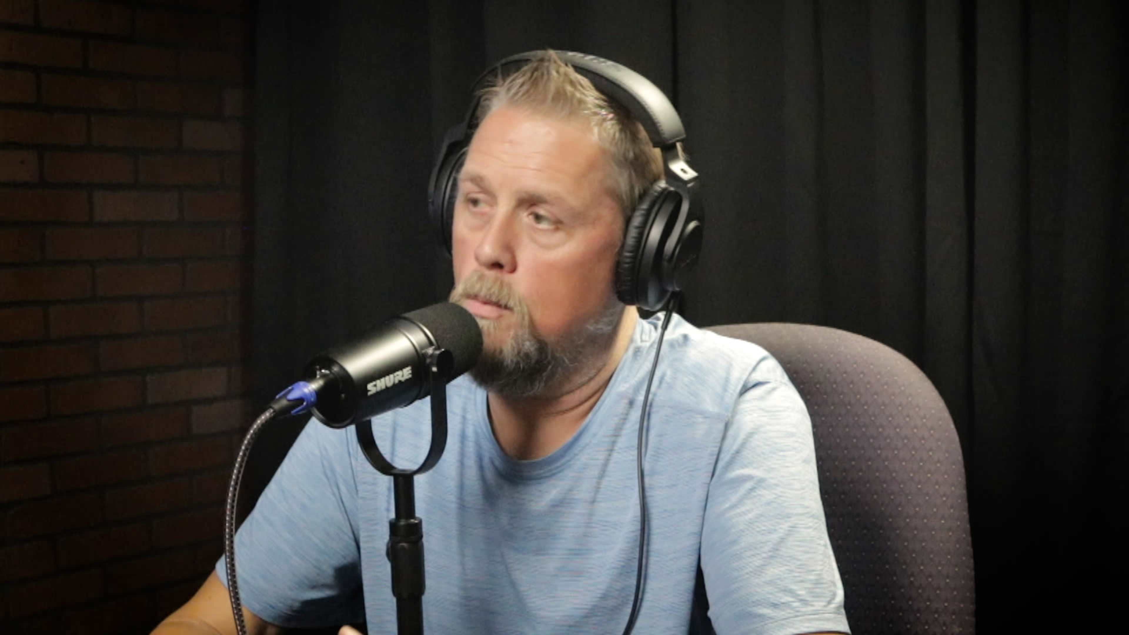 A man wearing headphones sits in front of a microphone during a recording session.